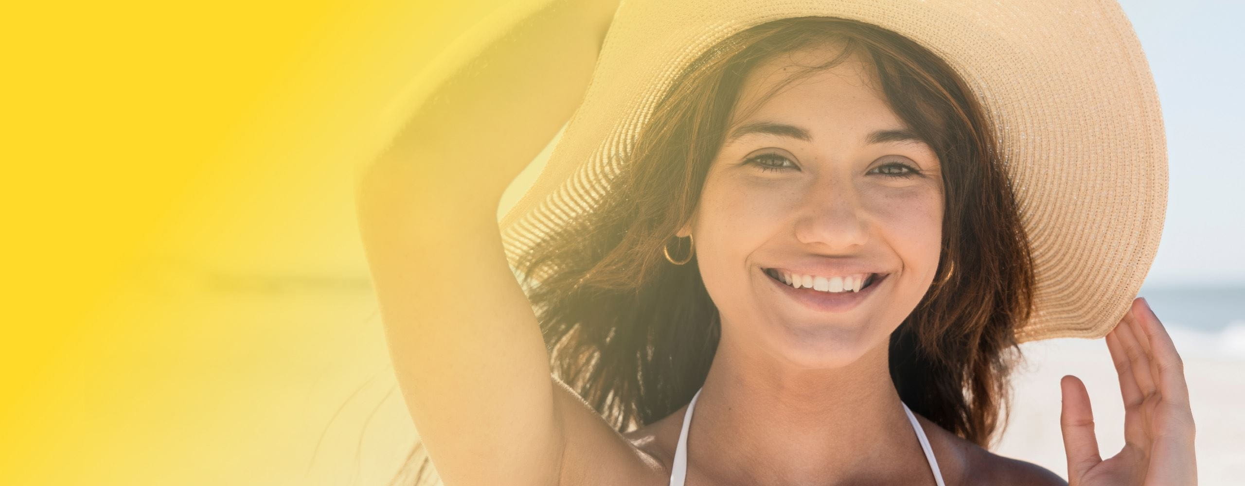 Femme qui sourit en tenant son chapeau à la plage