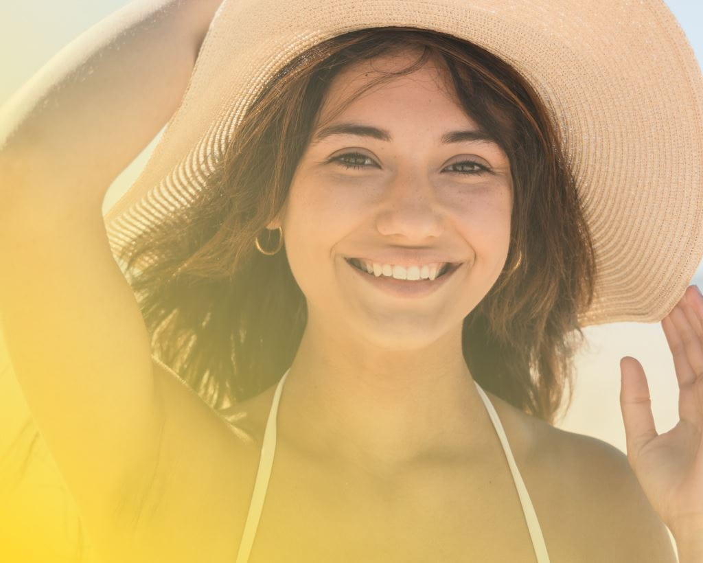 Smiling woman holding her hat at the beach