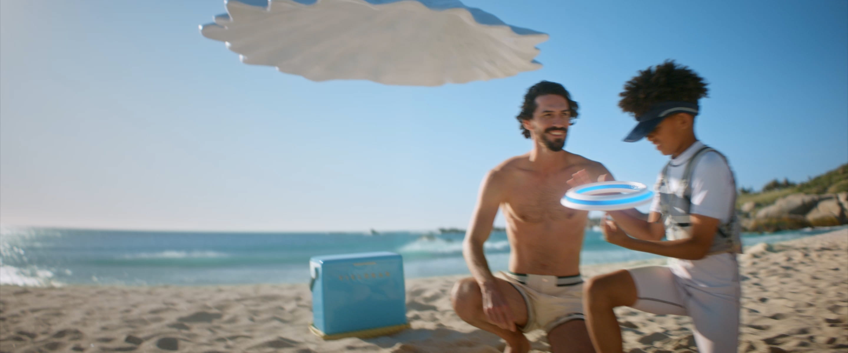 Video thumbnail prikazuje ženu kako diže ruku da se zaštiti od sunca na plaži, sa suncobranima u pozadini.