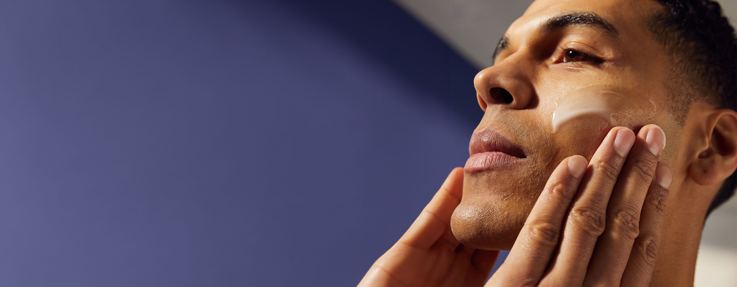 Vue d'une personne appliquant une crème NIVEA sur son visage tout en regardant au loin.