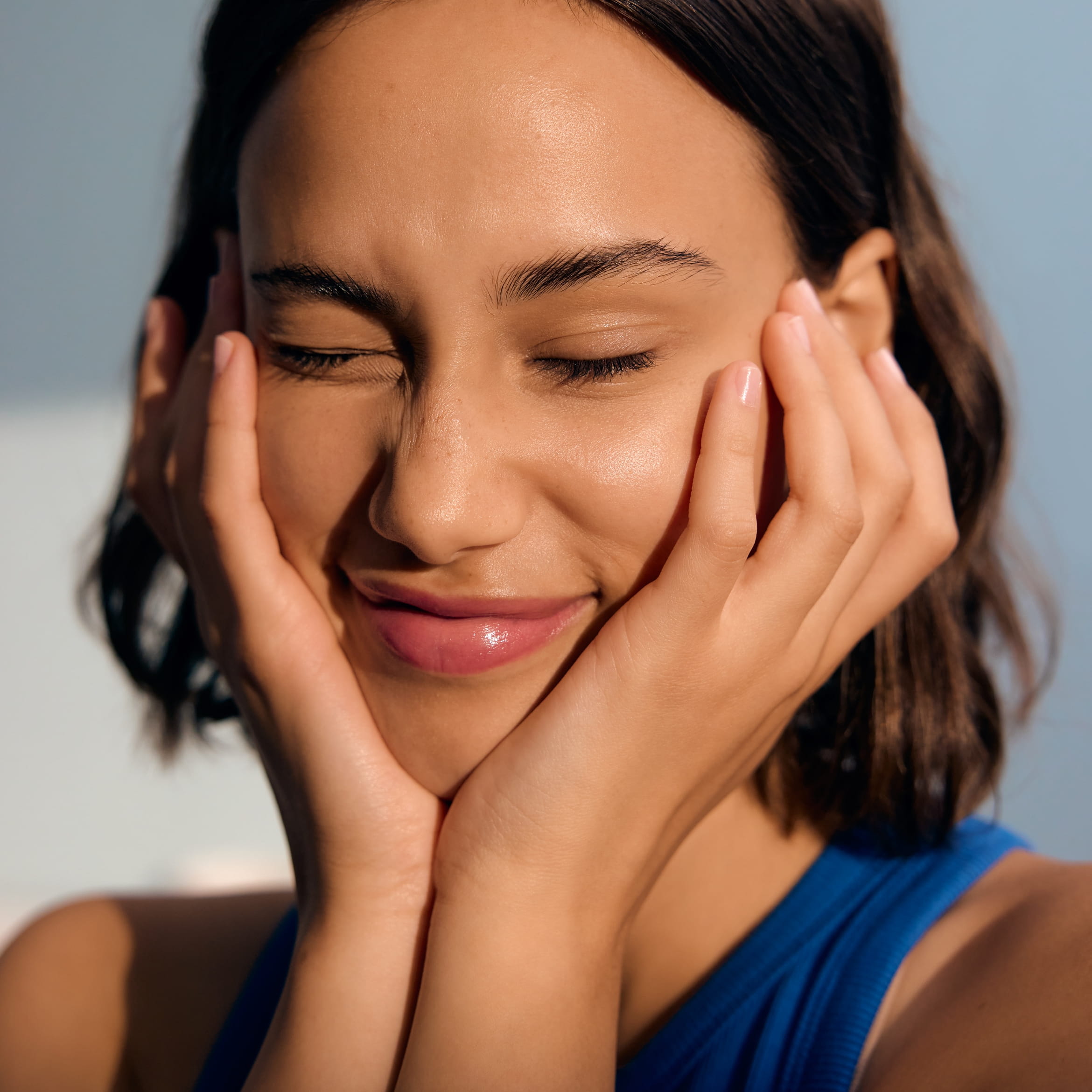 En person som blundar och håller händerna mot kinderna