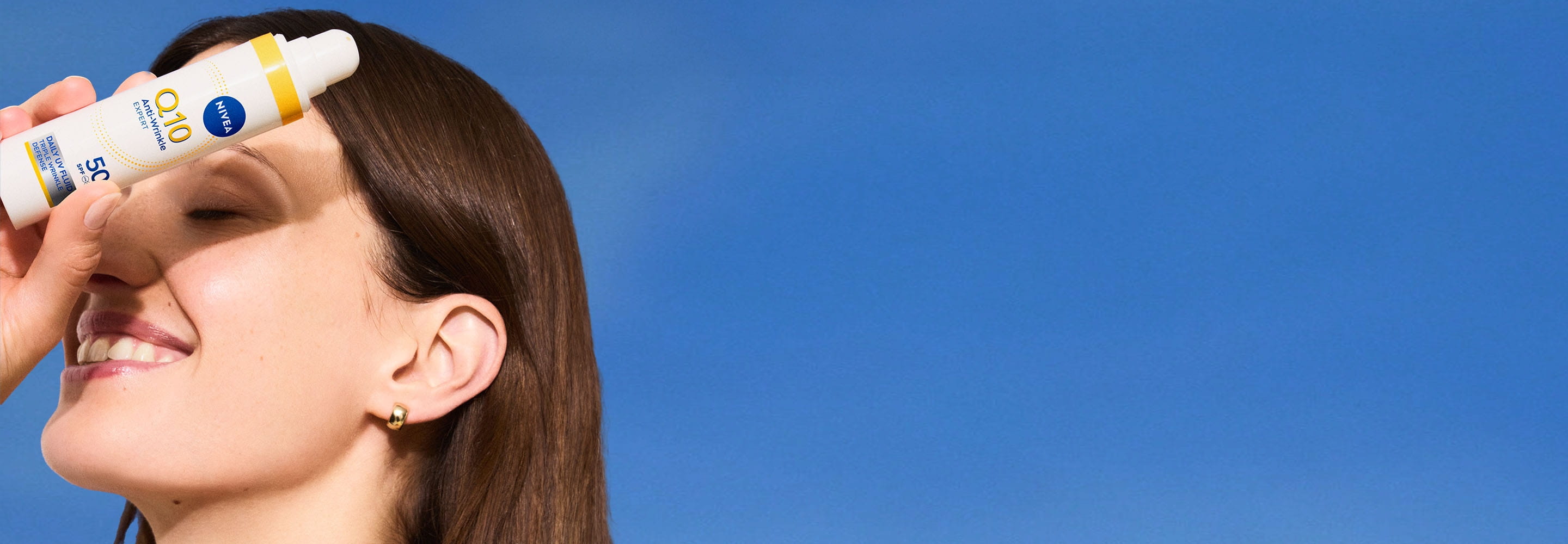 Nainen poseeraa NIVEA Q10 Daily UV Fluid -päivävoiteen kanssa, joka suojaa rypyiltä.