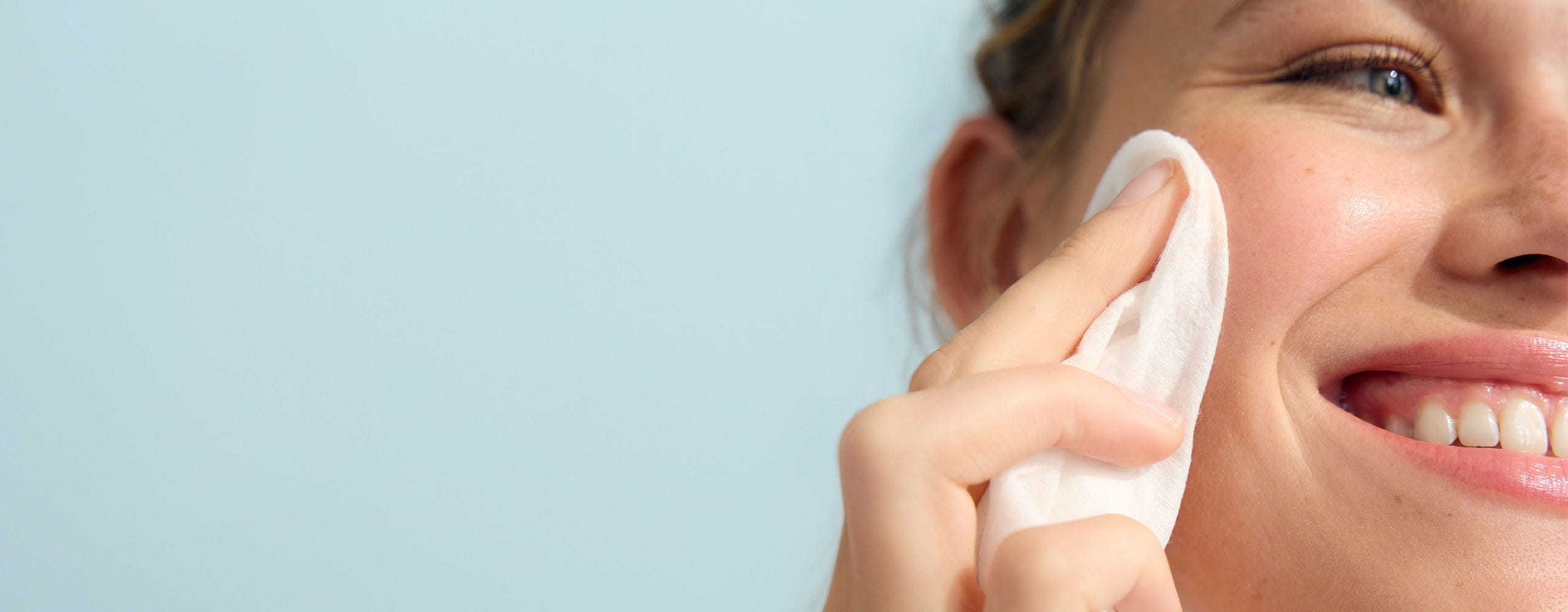 A person staring off into the distance while smiling and pressing a white coloured cloth against their face.