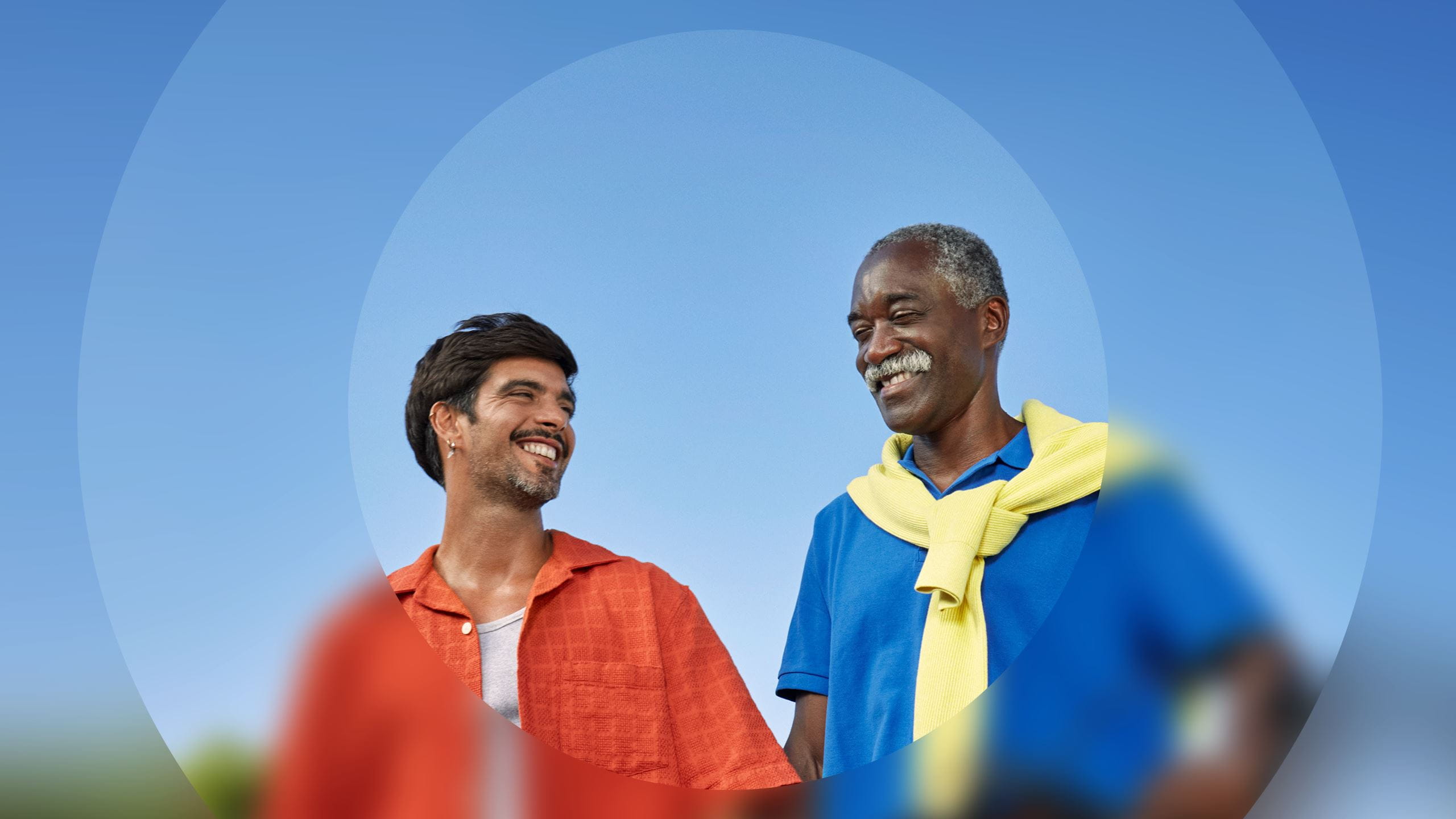 Younger and older men smiling at each other against a clear blue sky.