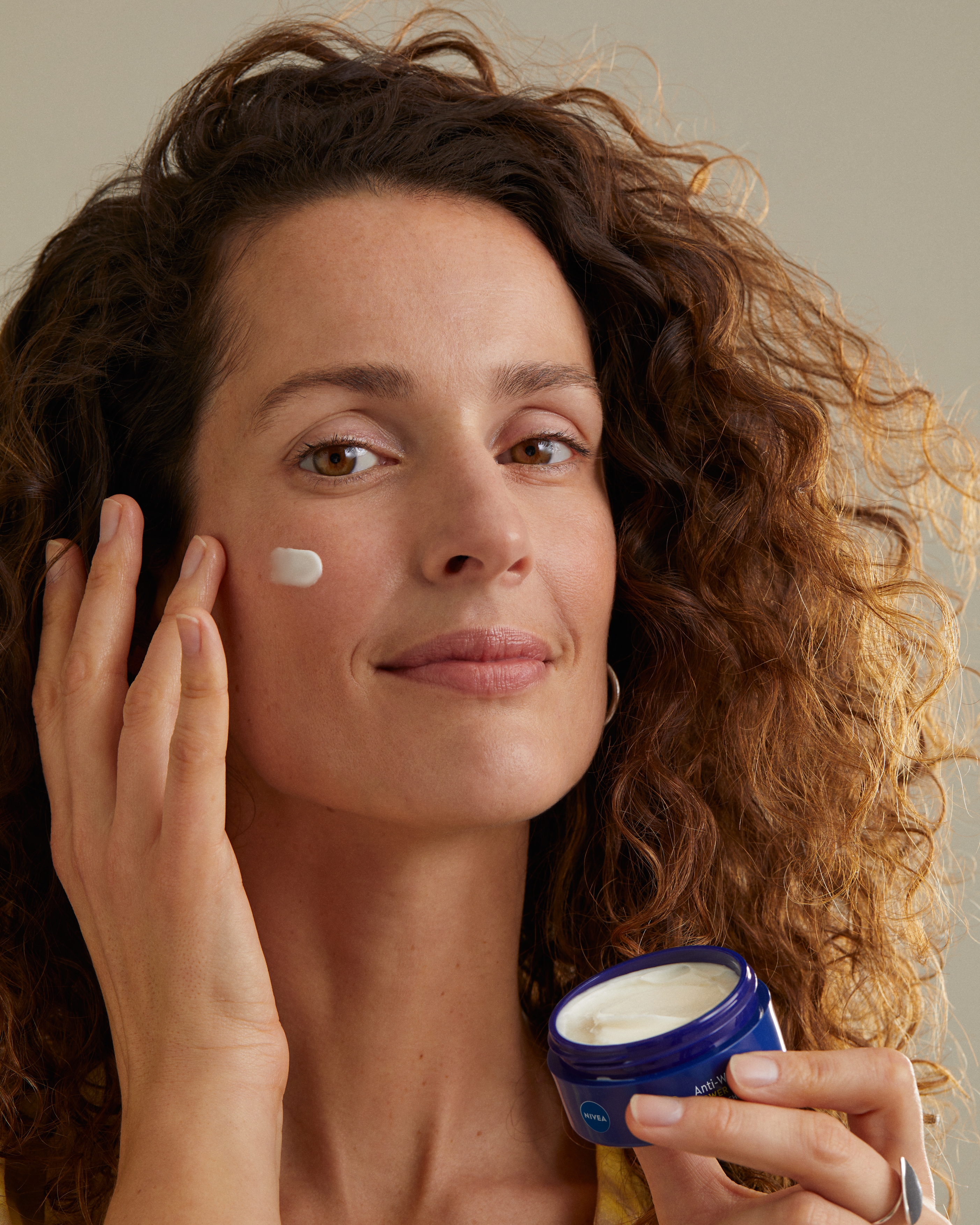 En person som applicerar nattkräm från en burk med ringfingret på kinden