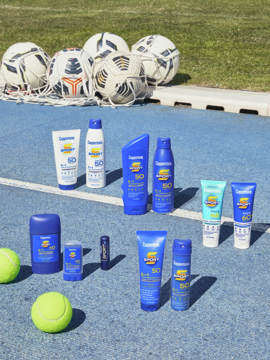 A collection of Coppertone Sport sunscreen products on an outdoor track with tennis balls and soccer balls