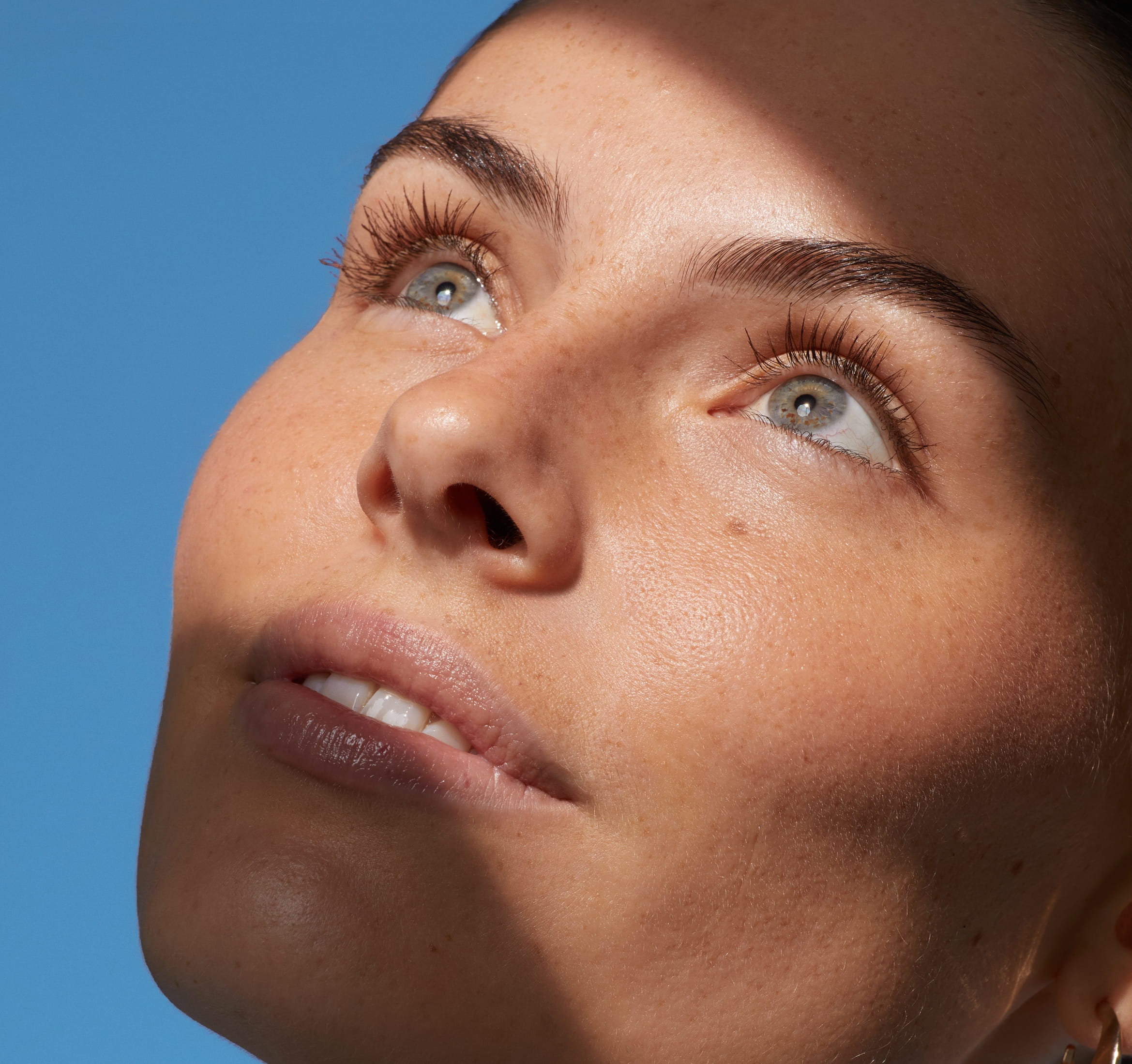 Person framför blå bakgrund tittar upp mot taket och ler