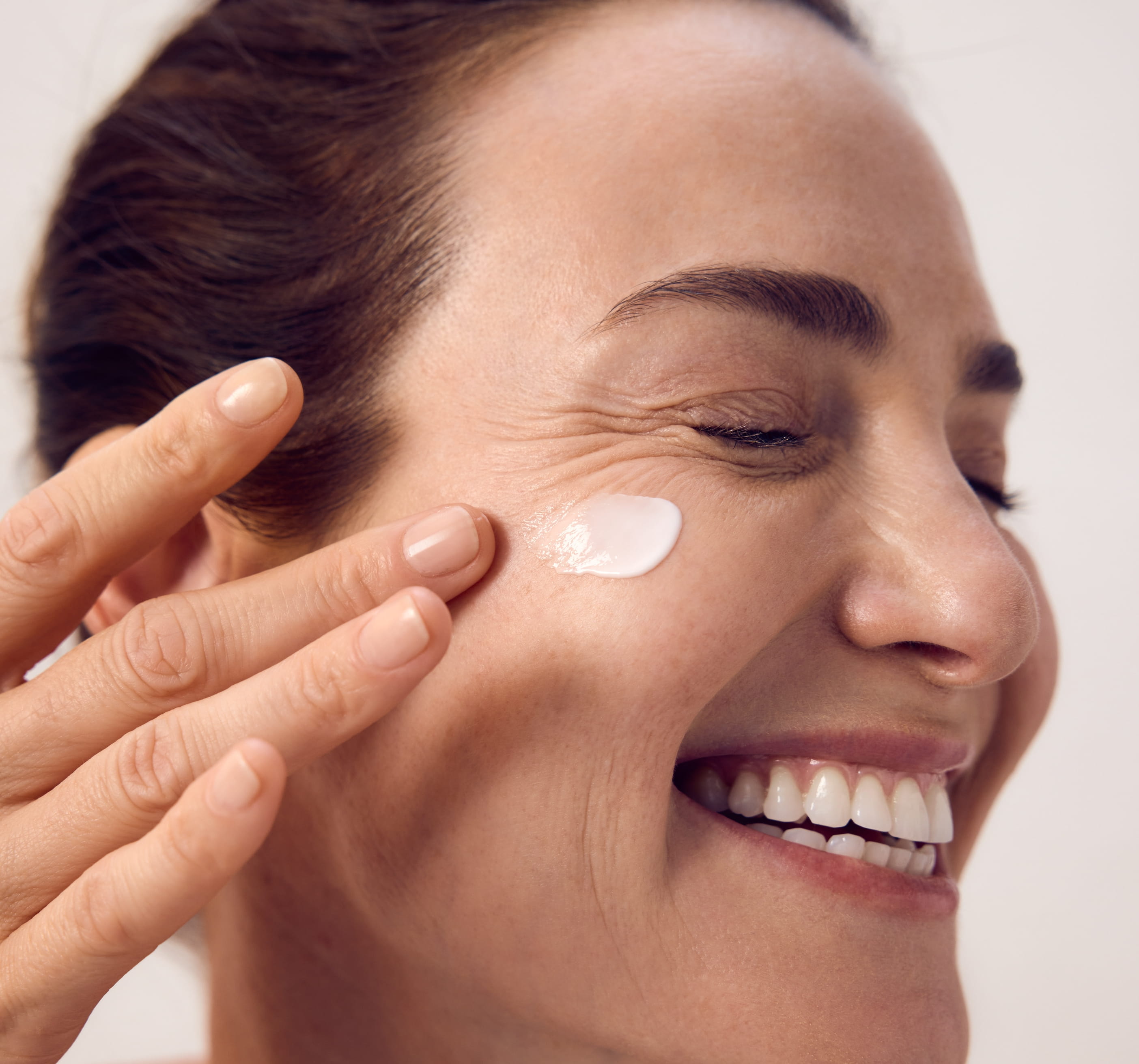 Kvinna som applicerar kräm på kinden och blundar och ler