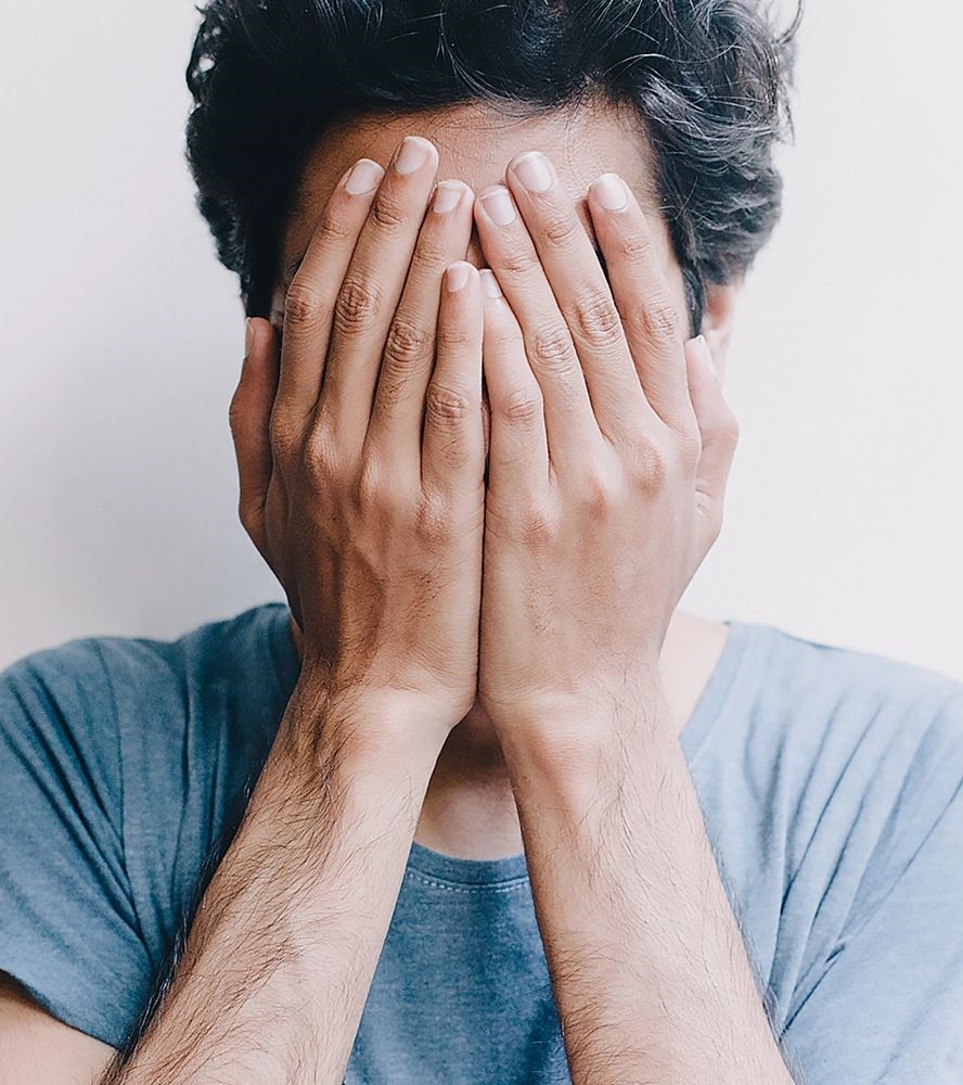 homem tampando o rosto com as mãos