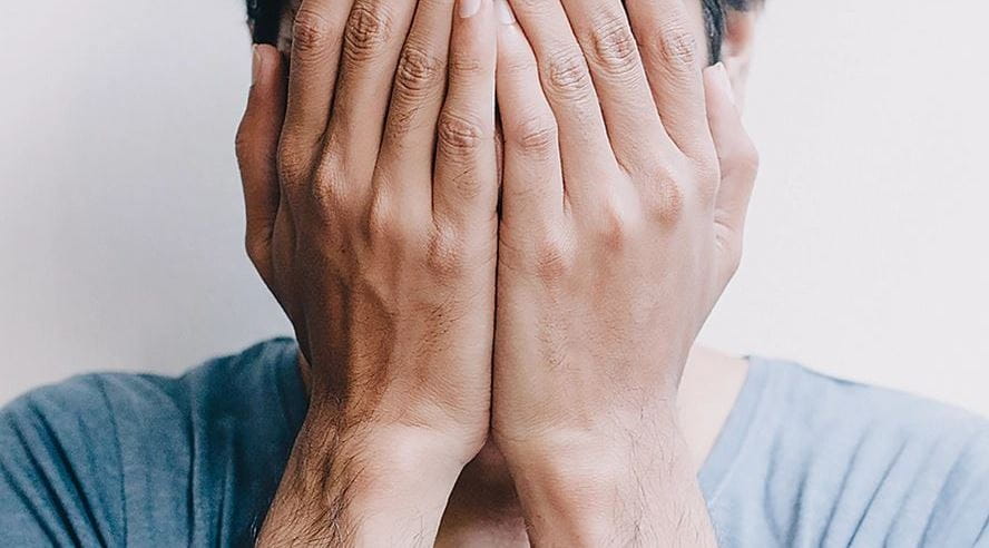 homem tampando o rosto com as mãos