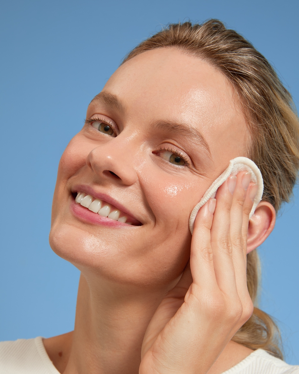 Blonde junge Frau, die mit einem Wattepad ein flüssiges Peeling aufträgt