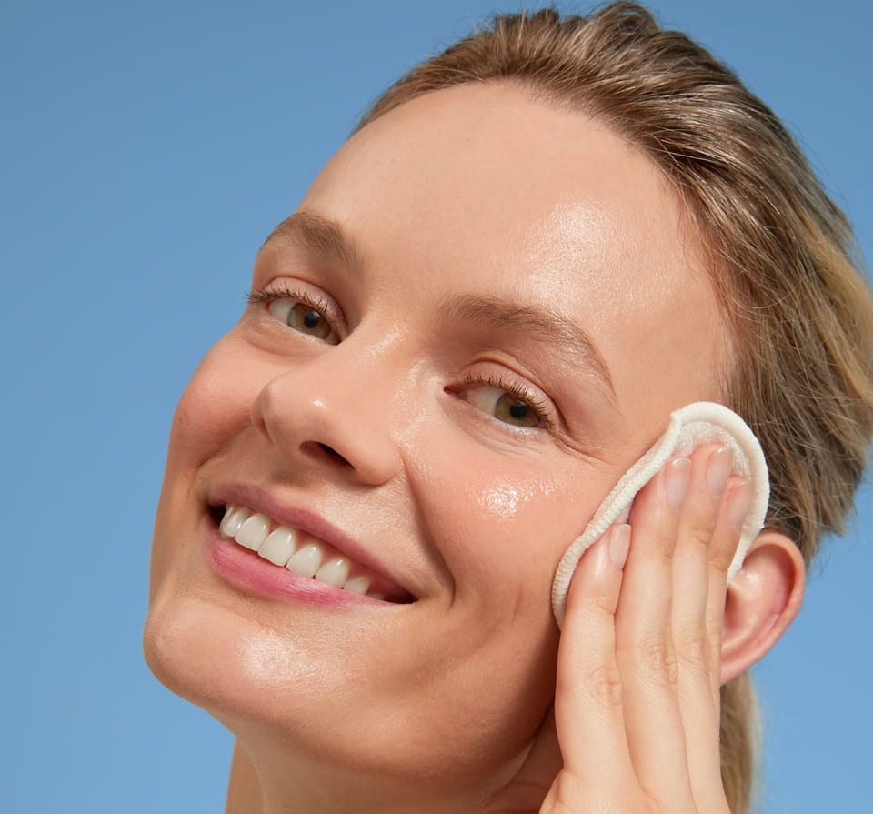 Blonde junge Frau, die mit einem Wattepad ein flüssiges Peeling aufträgt
