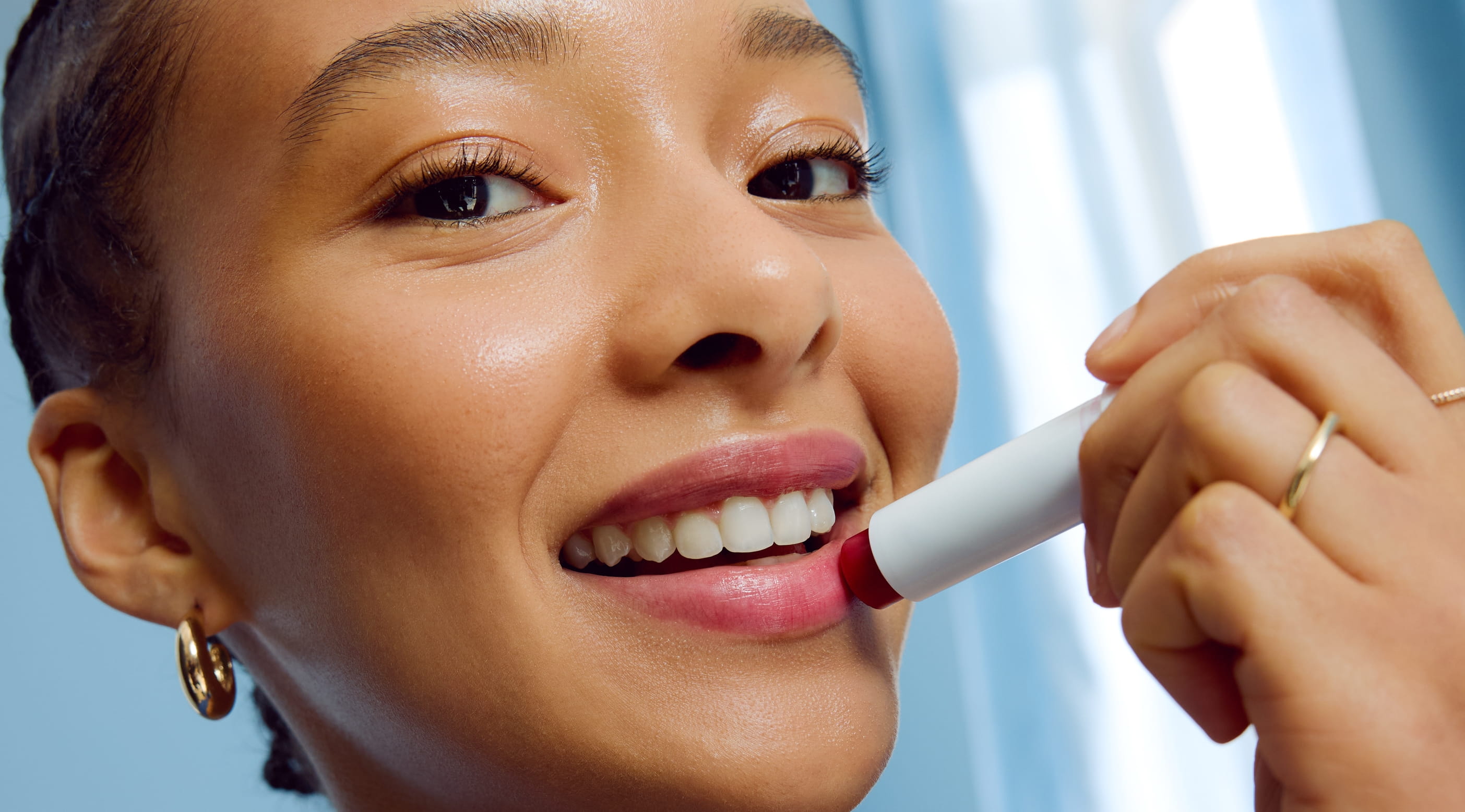 En person som tittar in i kameran och applicerar läppcerat