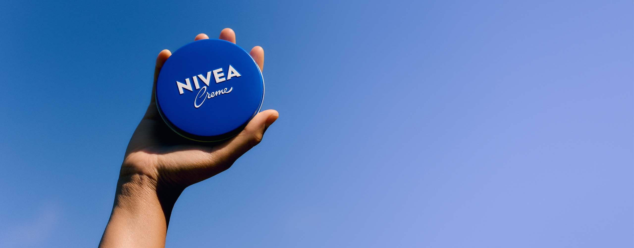 A NIVEA Creme product being held in someone's hand up towards the sky.