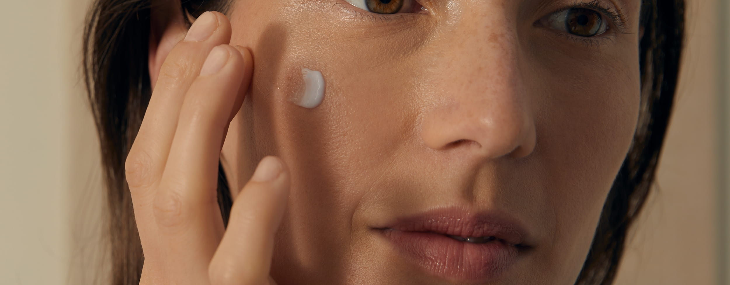 Eine lächelnde Frau, die sich Creme ins Gesicht aufträg