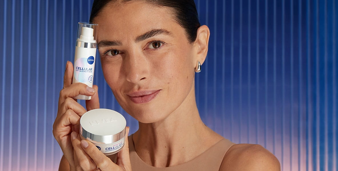 Uśmiechnięta kobieta trzyma przy twarzy dwa produkty: serum NIVEA Epigenetics oraz Krem na Dzień.