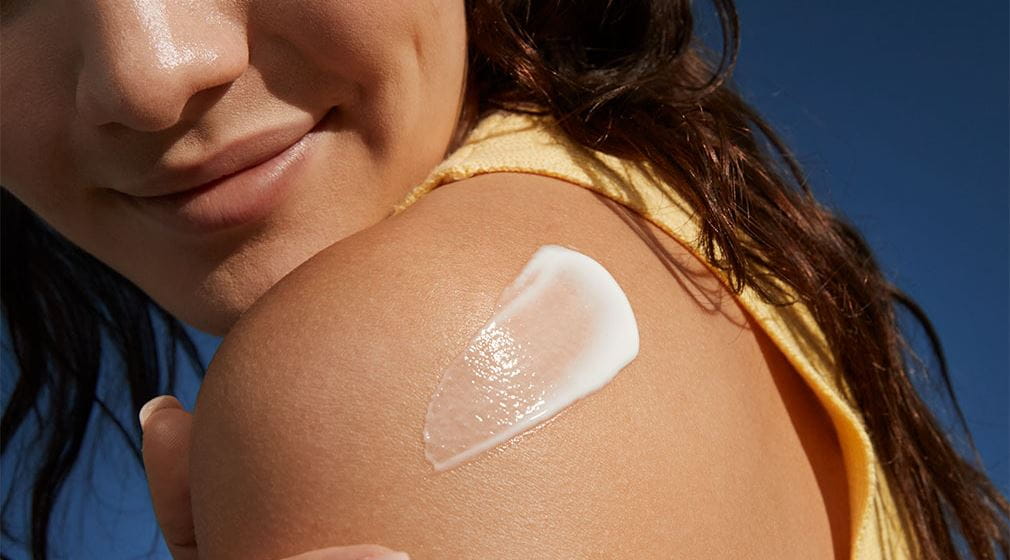 A woman peers over her shoulder while applying a NIVEA EXTRA BRIGHT vitamin body serum.