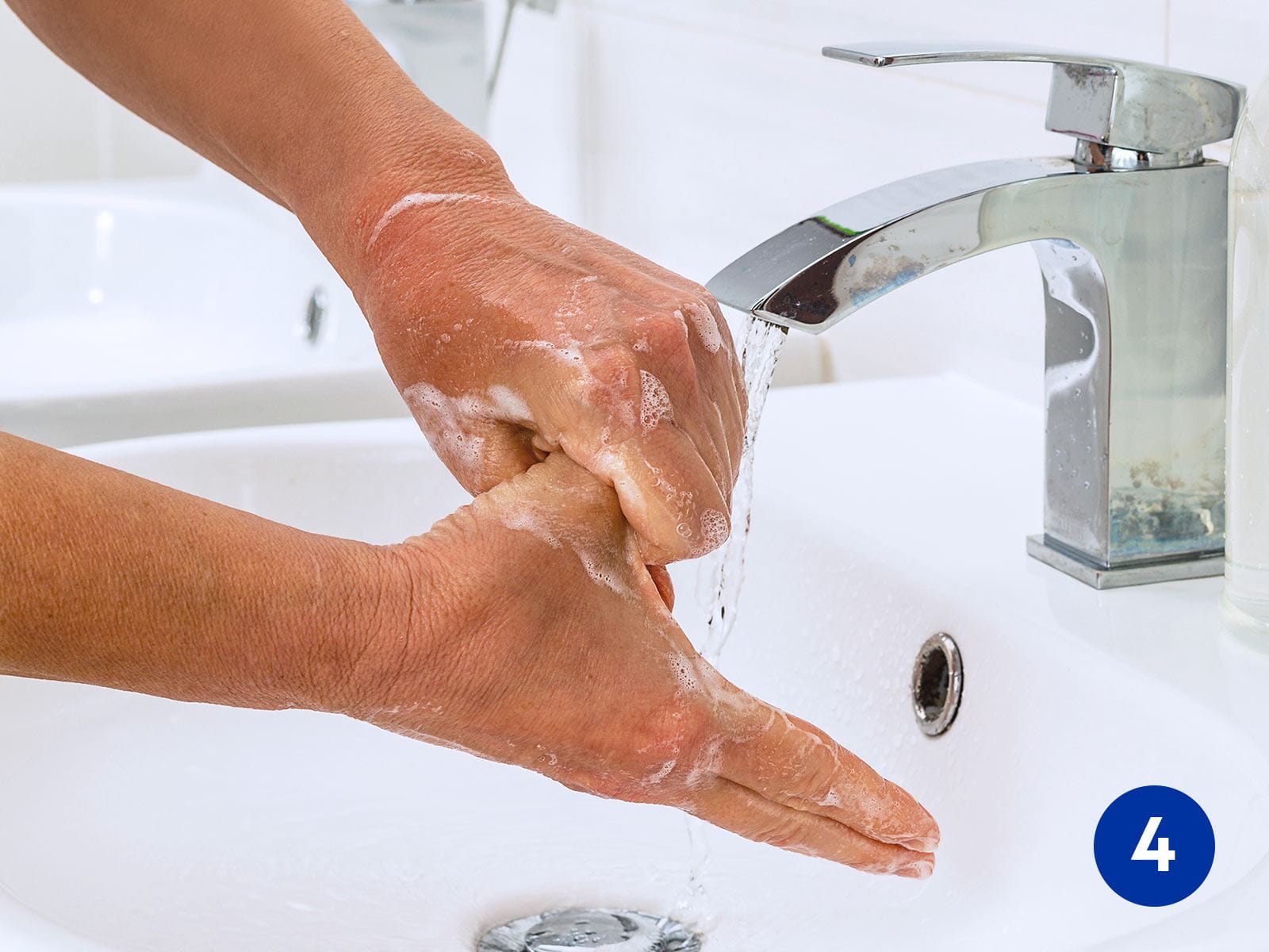 View of a person washing their hands with foaming soap in a sink.