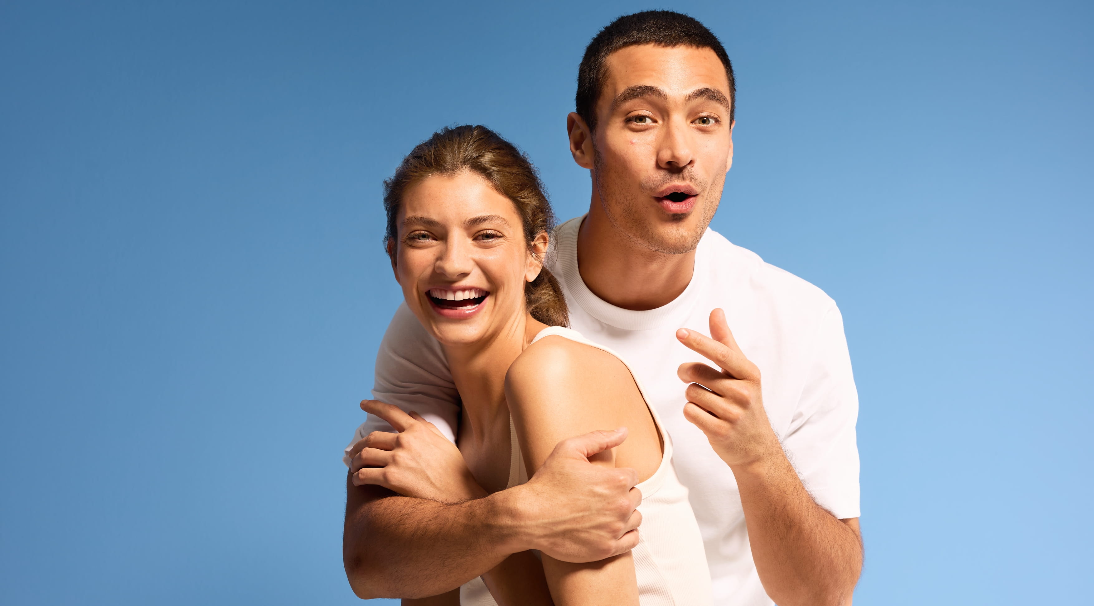 en tjej i vitt linne och en kille i vit t-shirt, framför blå bakgrund