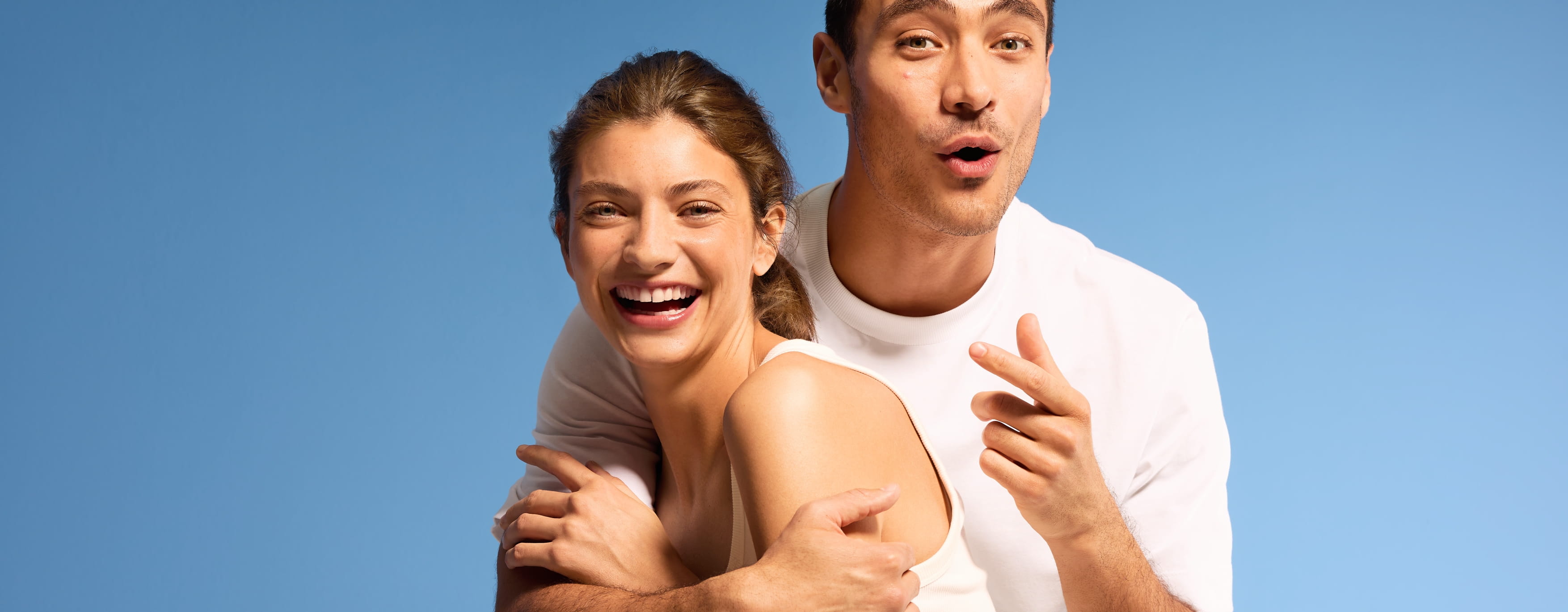 en tjej i vitt linne och en kille i vit t-shirt, framför blå bakgrund