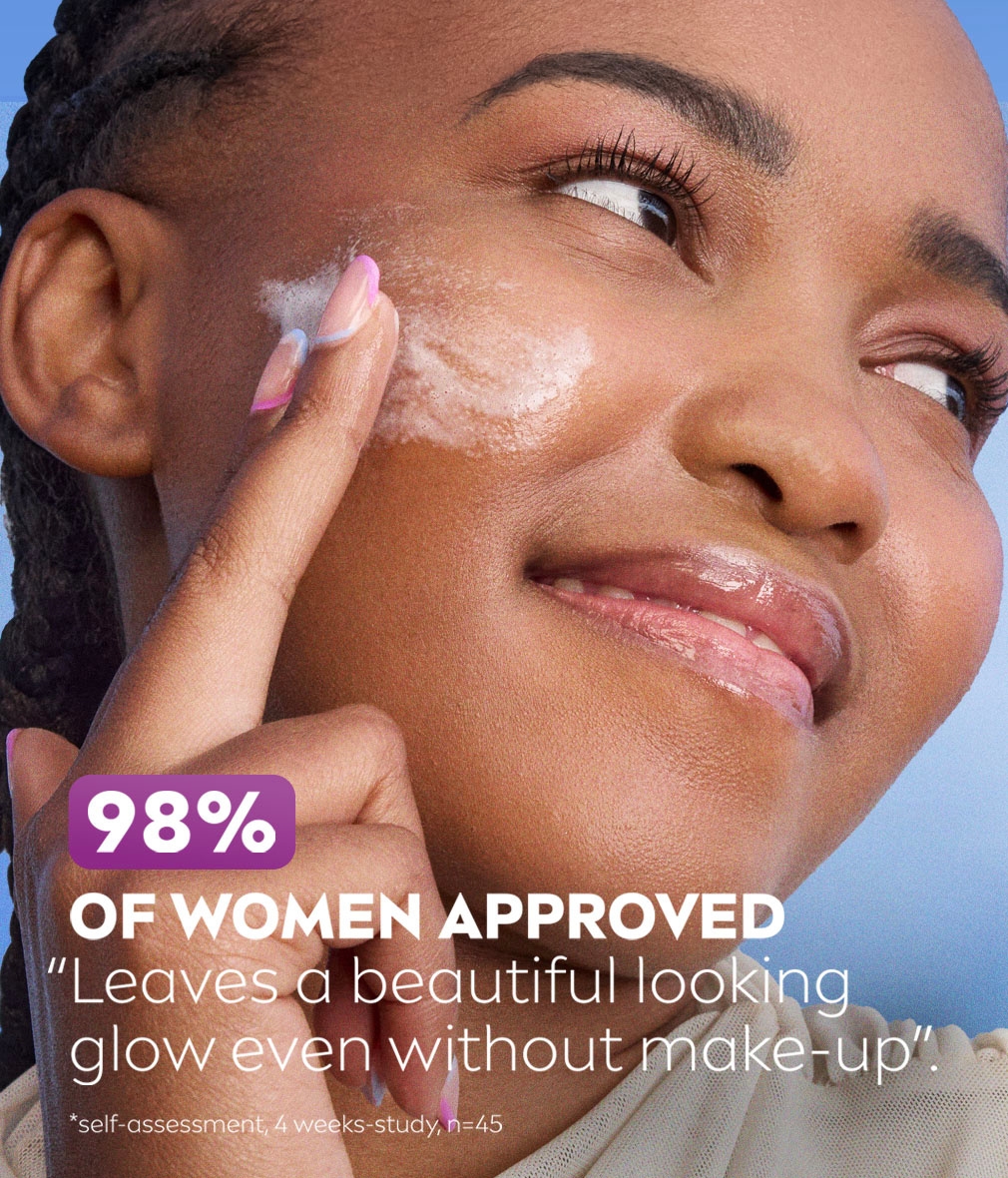 Young woman smiles to the side, while swiping Daily Fluid across her glowing cheek skin.