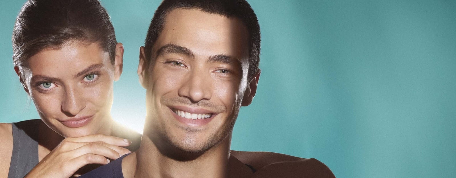 Primo piano di una donna e di un uomo: entrambi i loro volti mostrano una pelle chiara e priva di imperfezioni. Sorridono alla telecamera, su uno sfondo verde.