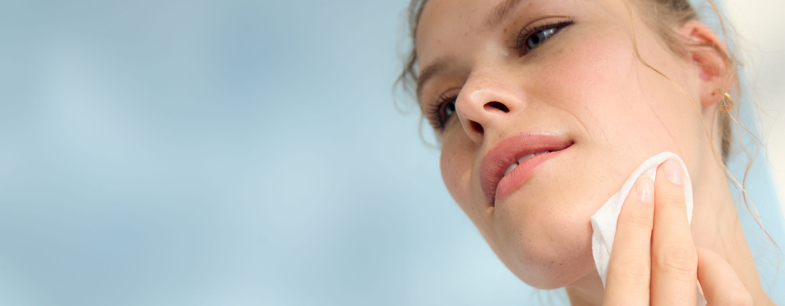 View of a person pressing a face wipe over their eye to show removing their eye makeup.
