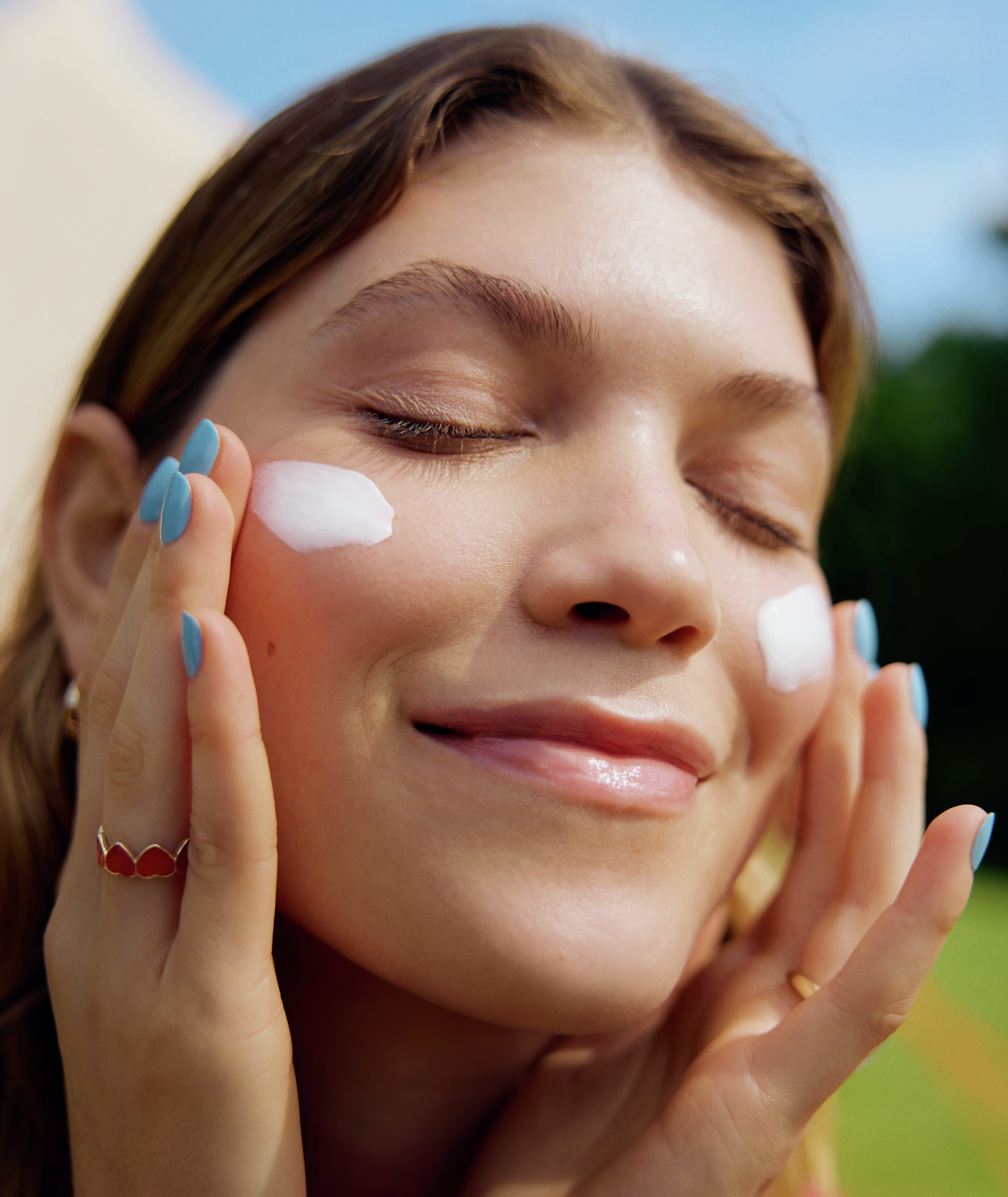 kvinna som blundar och applicerar kräm på båda kinderna