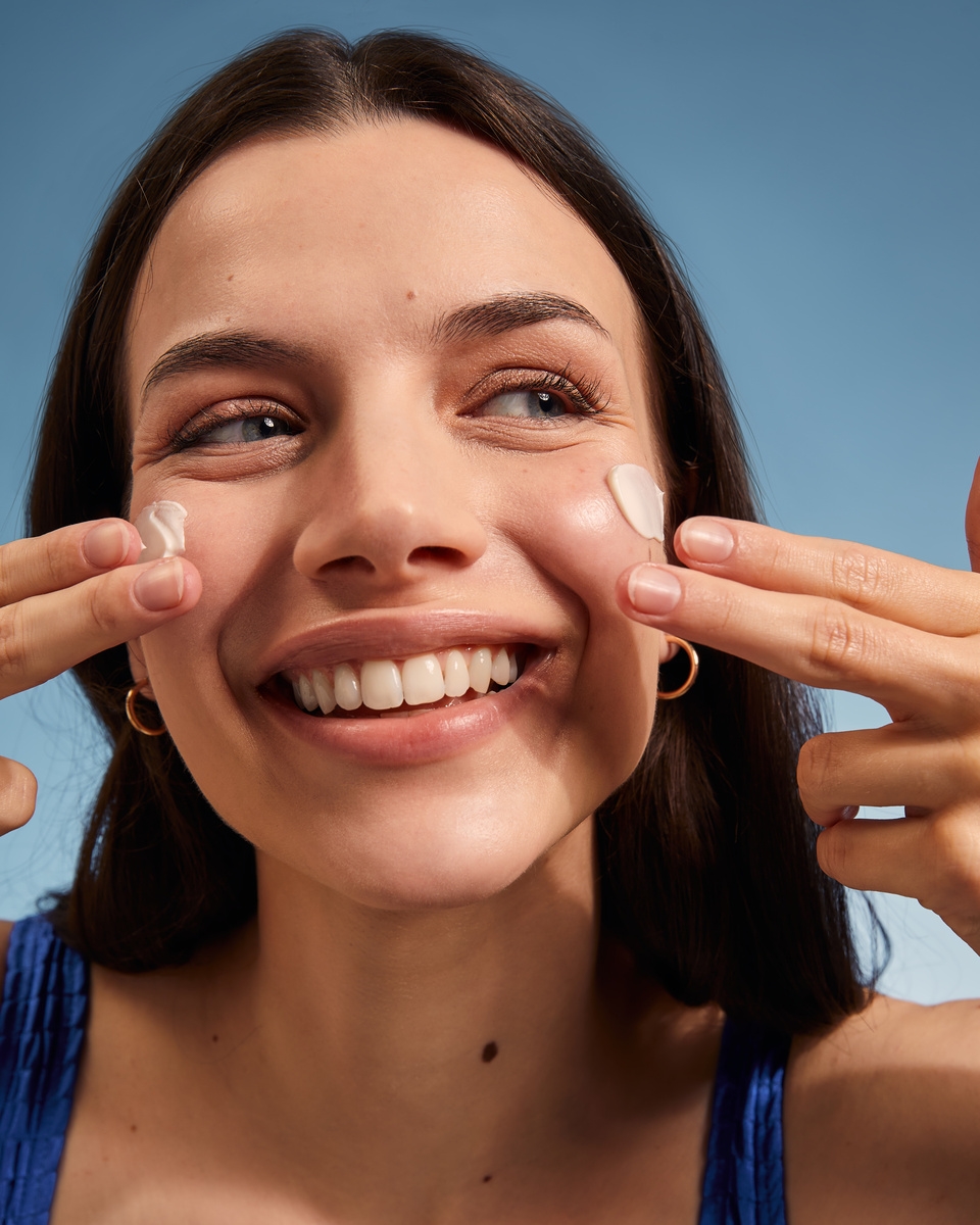Smiling woman applying sunscreen cream to her cheeks