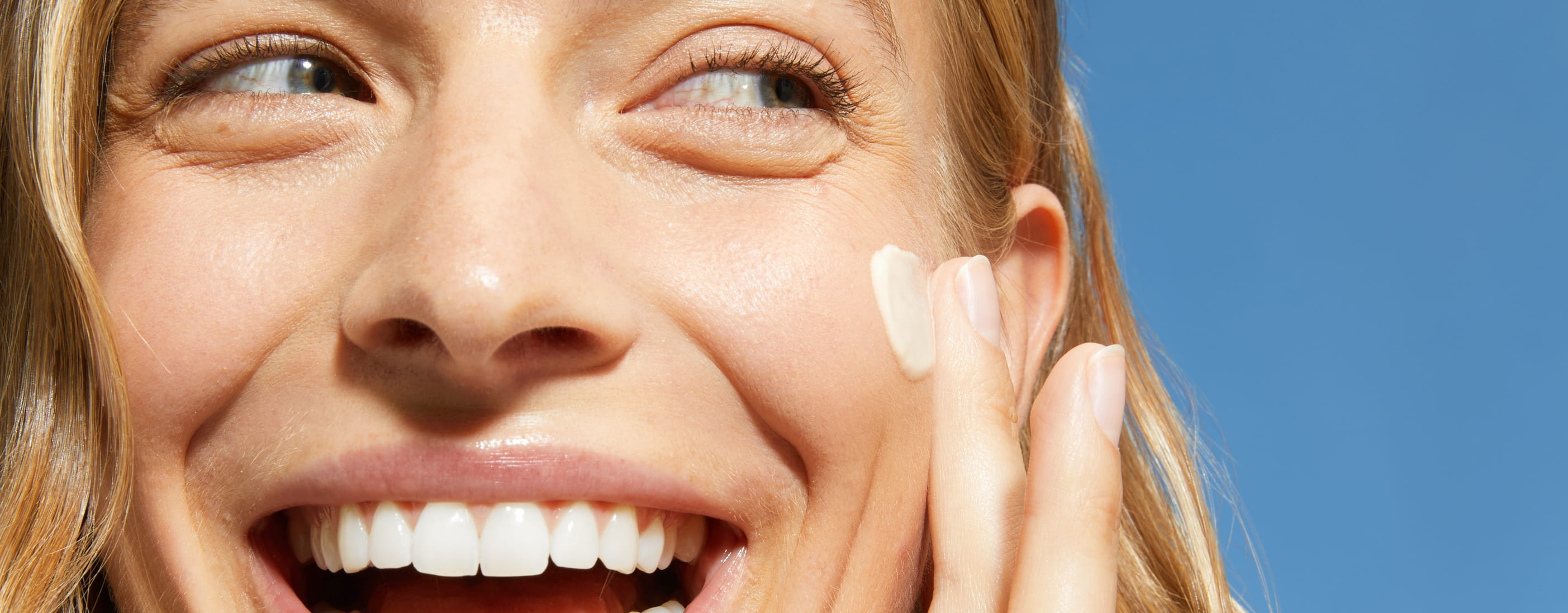 glad kvinna som applicerar kräm på kinden