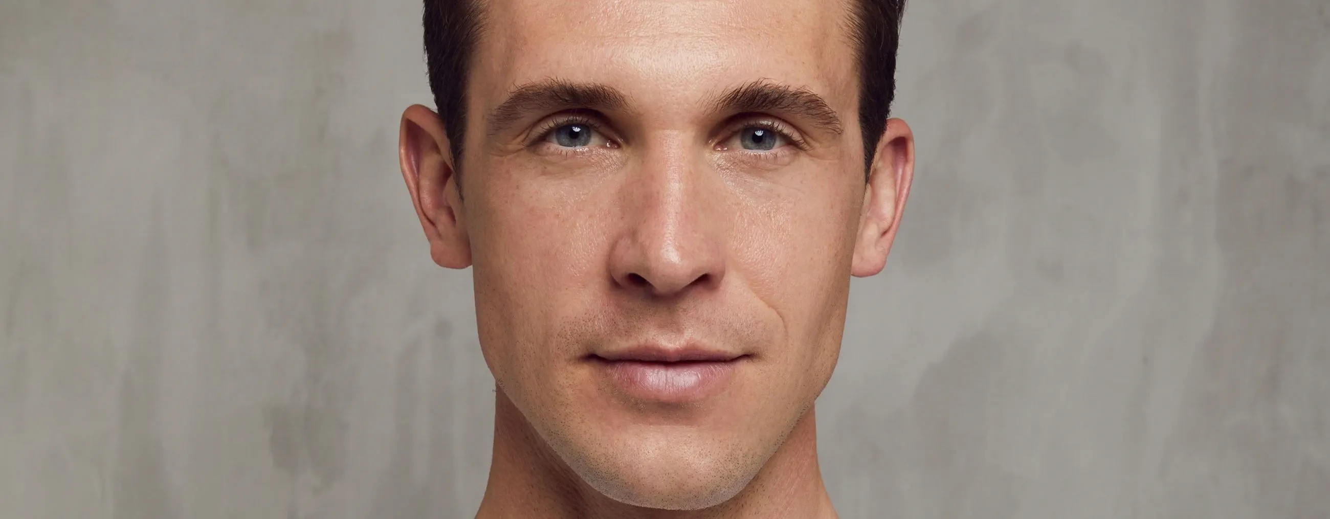 Un homme souriant sur un fond gris