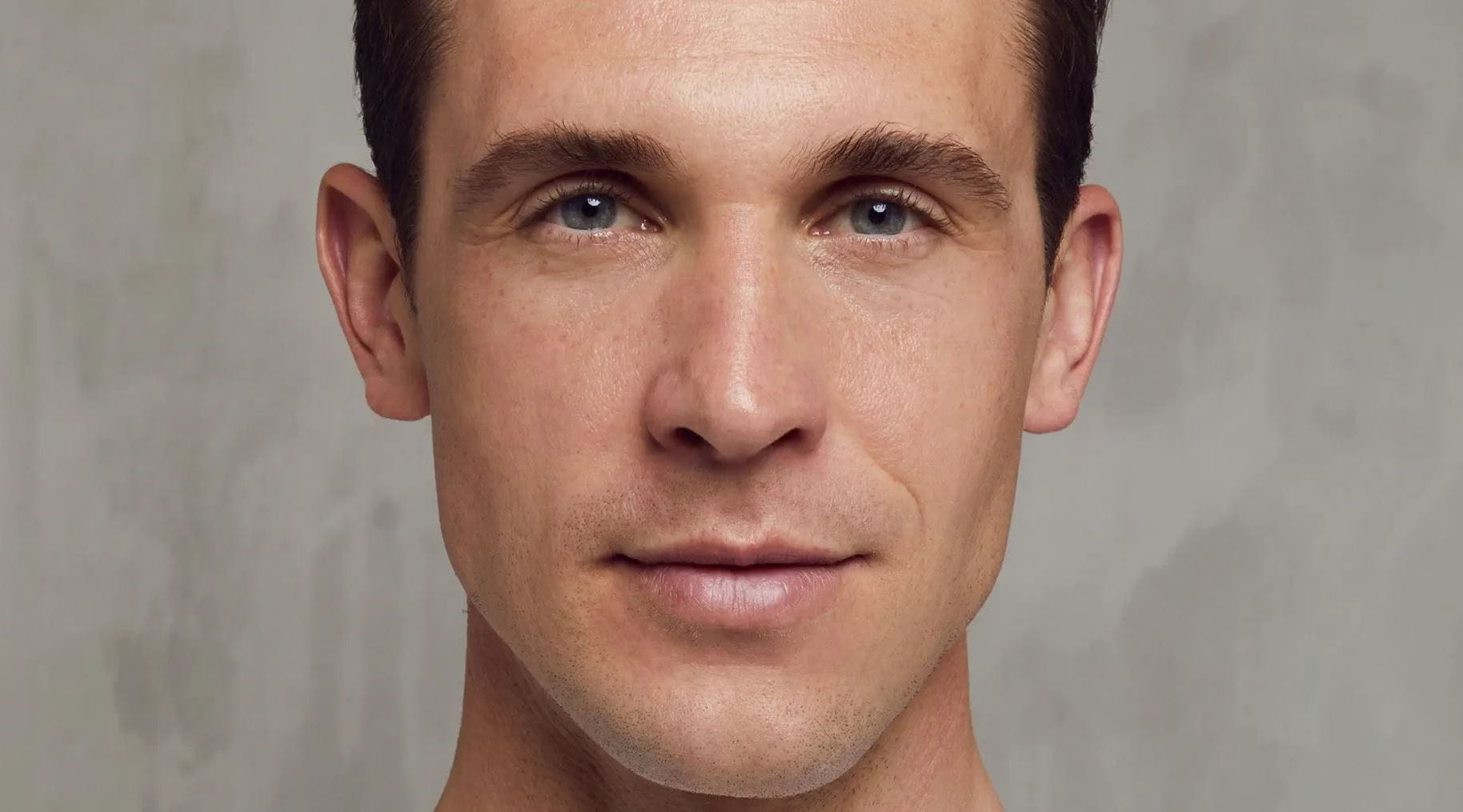 Un homme souriant sur un fond gris