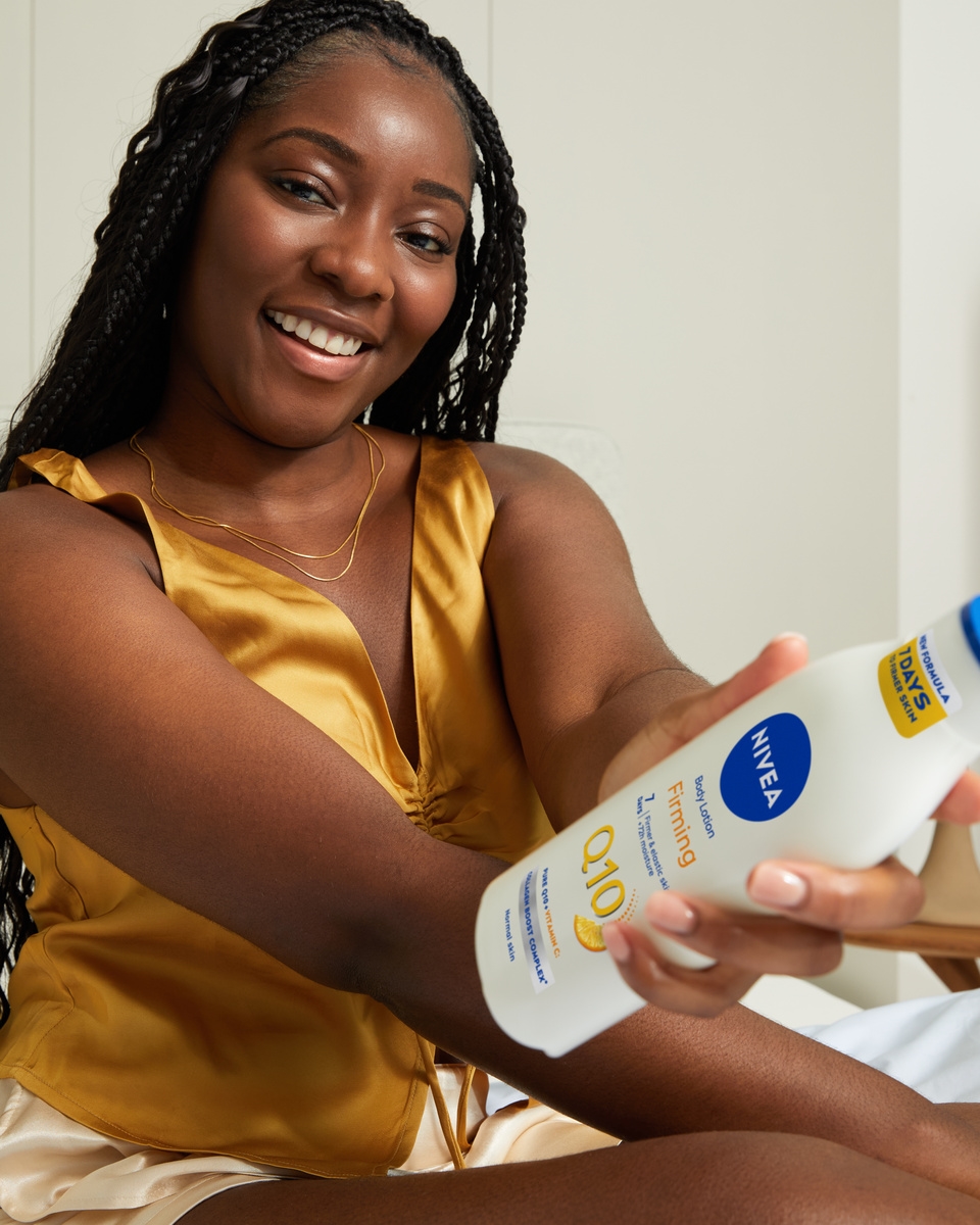 Młoda czarna kobieta używająca serum-balsamu ujędrniającego i energetyzującego Q10 Firming+ Energising Body Serum-Lotion