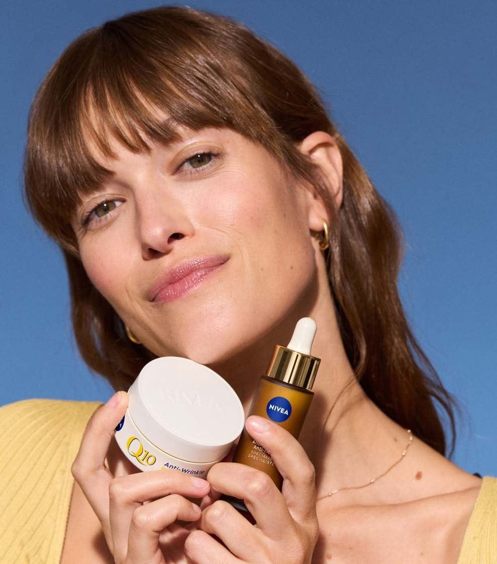Une femme vêtue d'un haut jaune ouvre un flacon de NIVEA Q10 ANTI-RIDES SPÉCIALISTE SÉRUM DOUBLE ACTION
