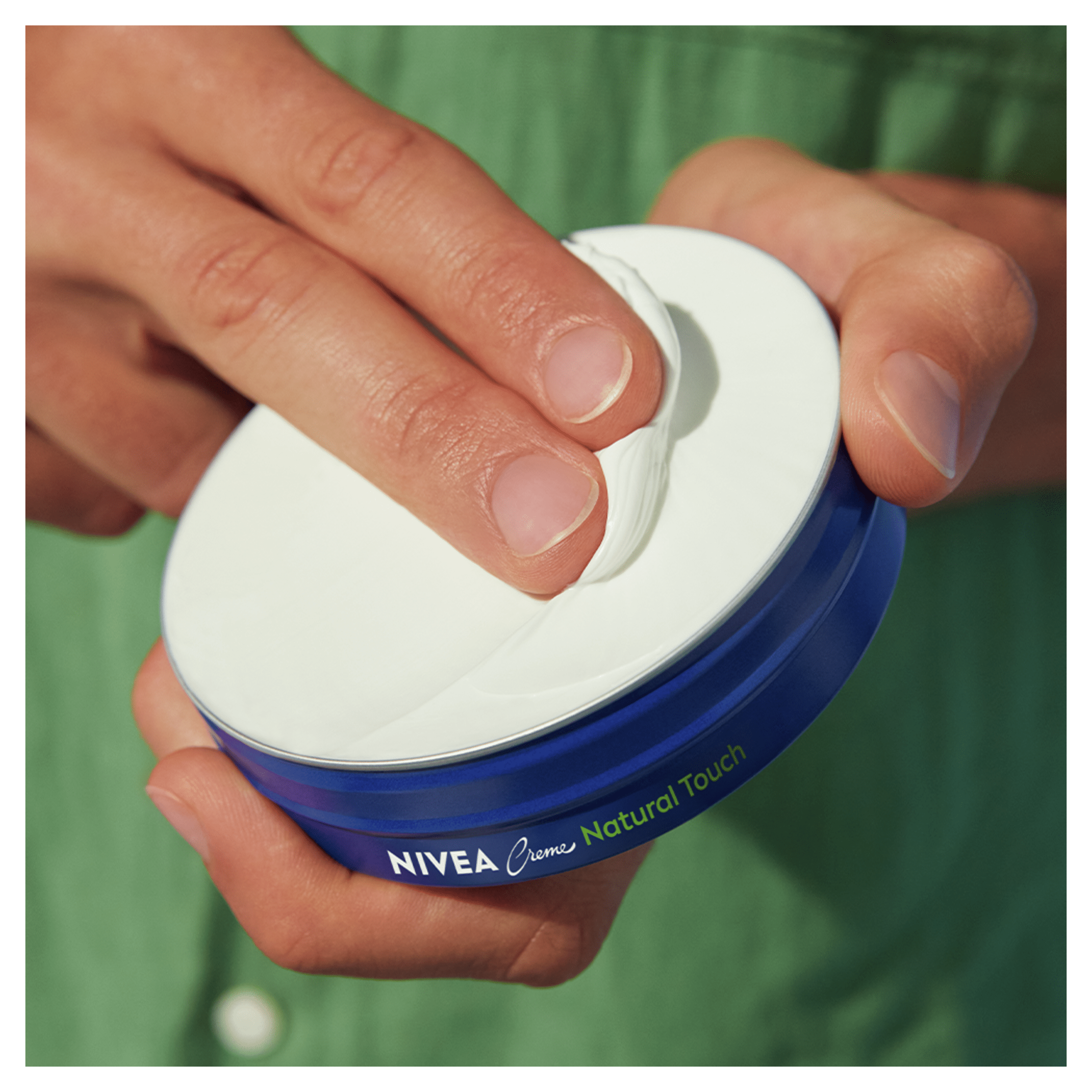 Hand scooping NIVEA Creme Natural Touch from blue tin.