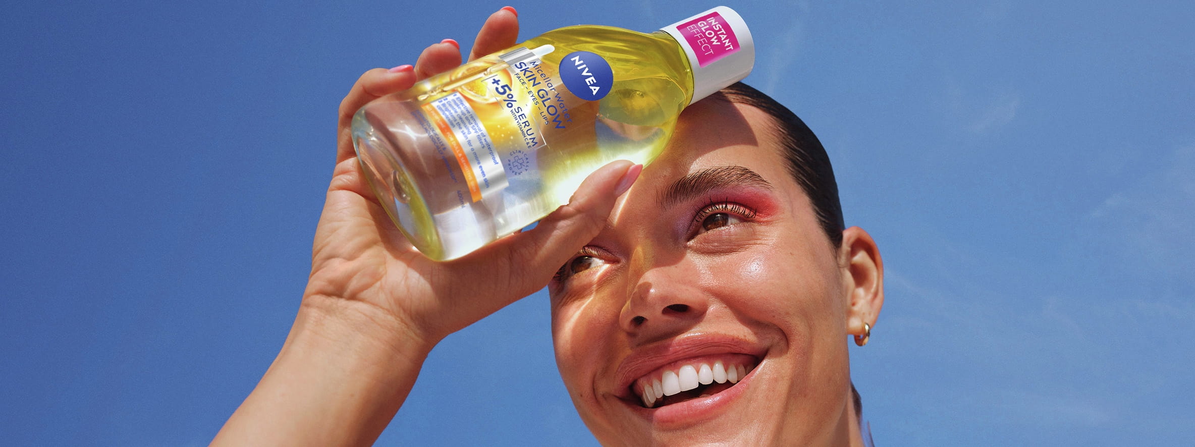 Smiling woman with pink eyeshadow touches her face, next to NIVEA Serum-infused Micellar Water