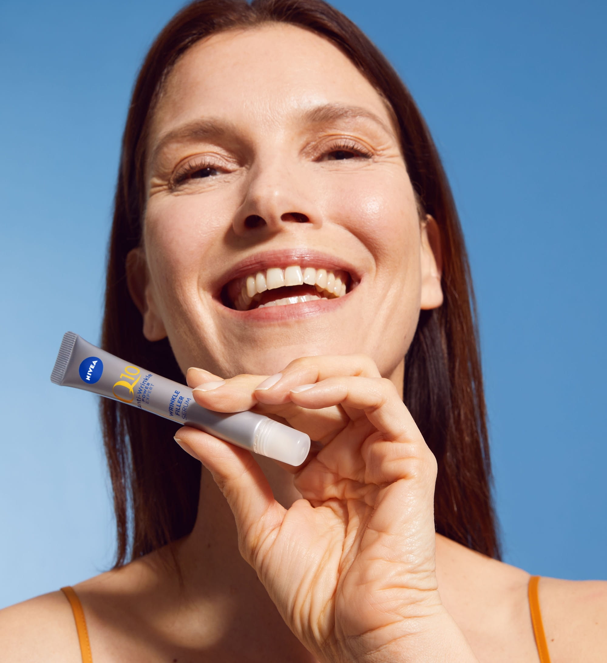 En person som ler och håller i en NIVEA Q10 Power Wrinkle Filler Serum