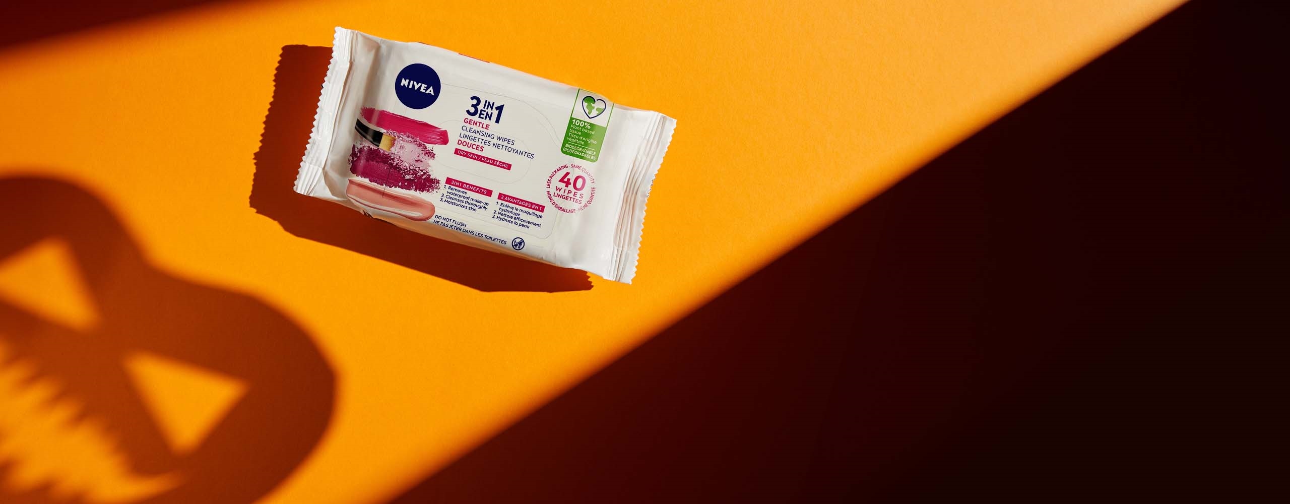 A NIVEA 3 in 1 gentle cleansing wipes package shown face up on an orange coloured table with shadows surrounding it.