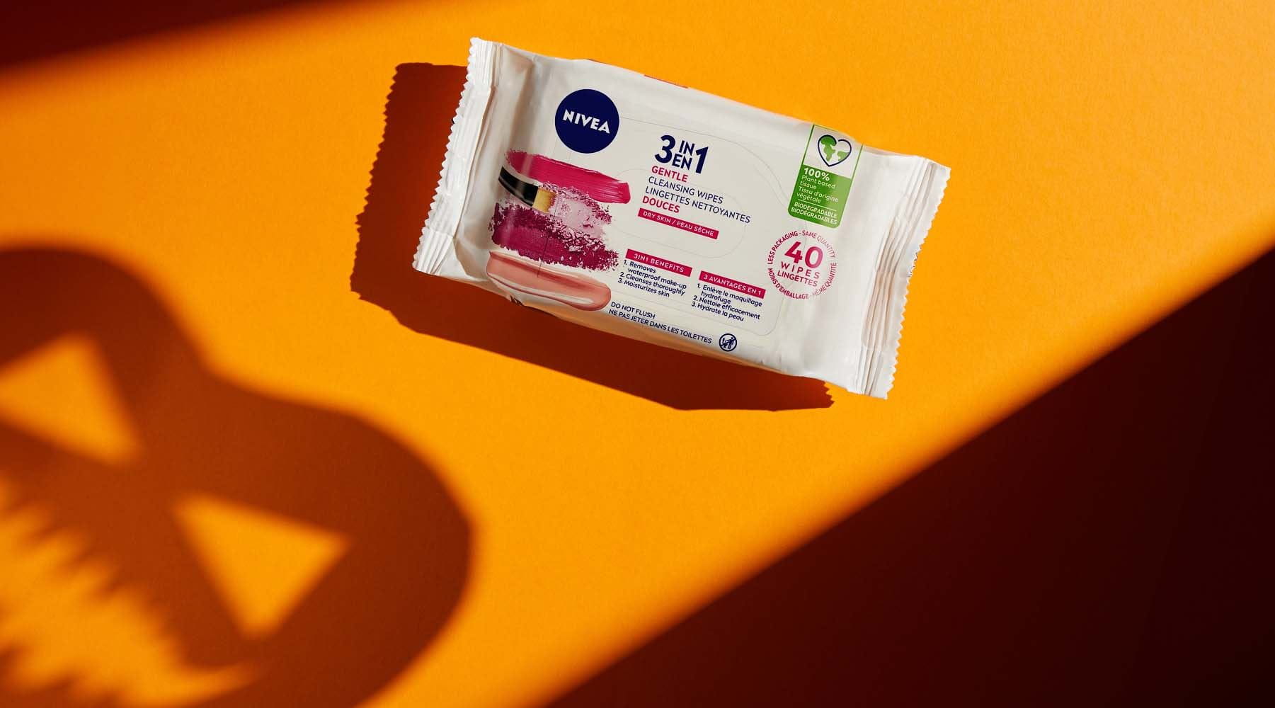 A NIVEA 3 in 1 gentle cleansing wipes package shown face up on an orange coloured table with shadows surrounding it.