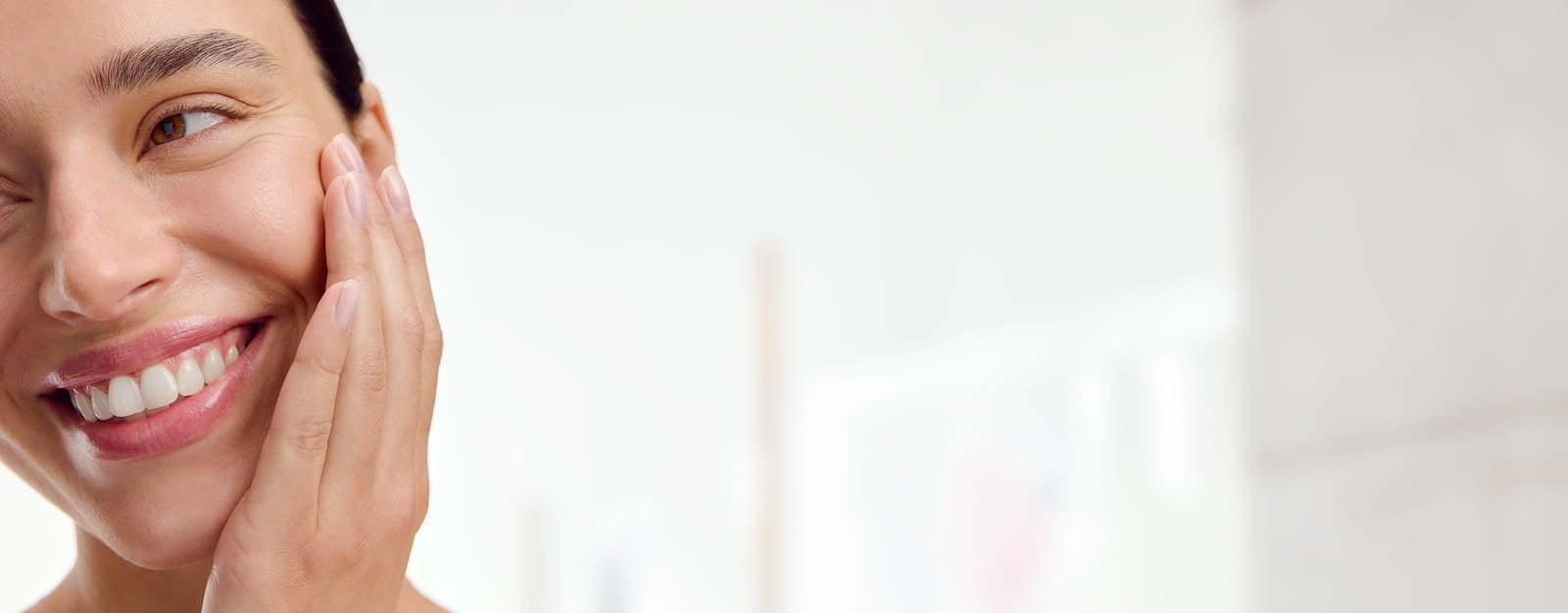 Gros plan d'une personne souriant en tenant son visage dans sa main, sur fond blanc.