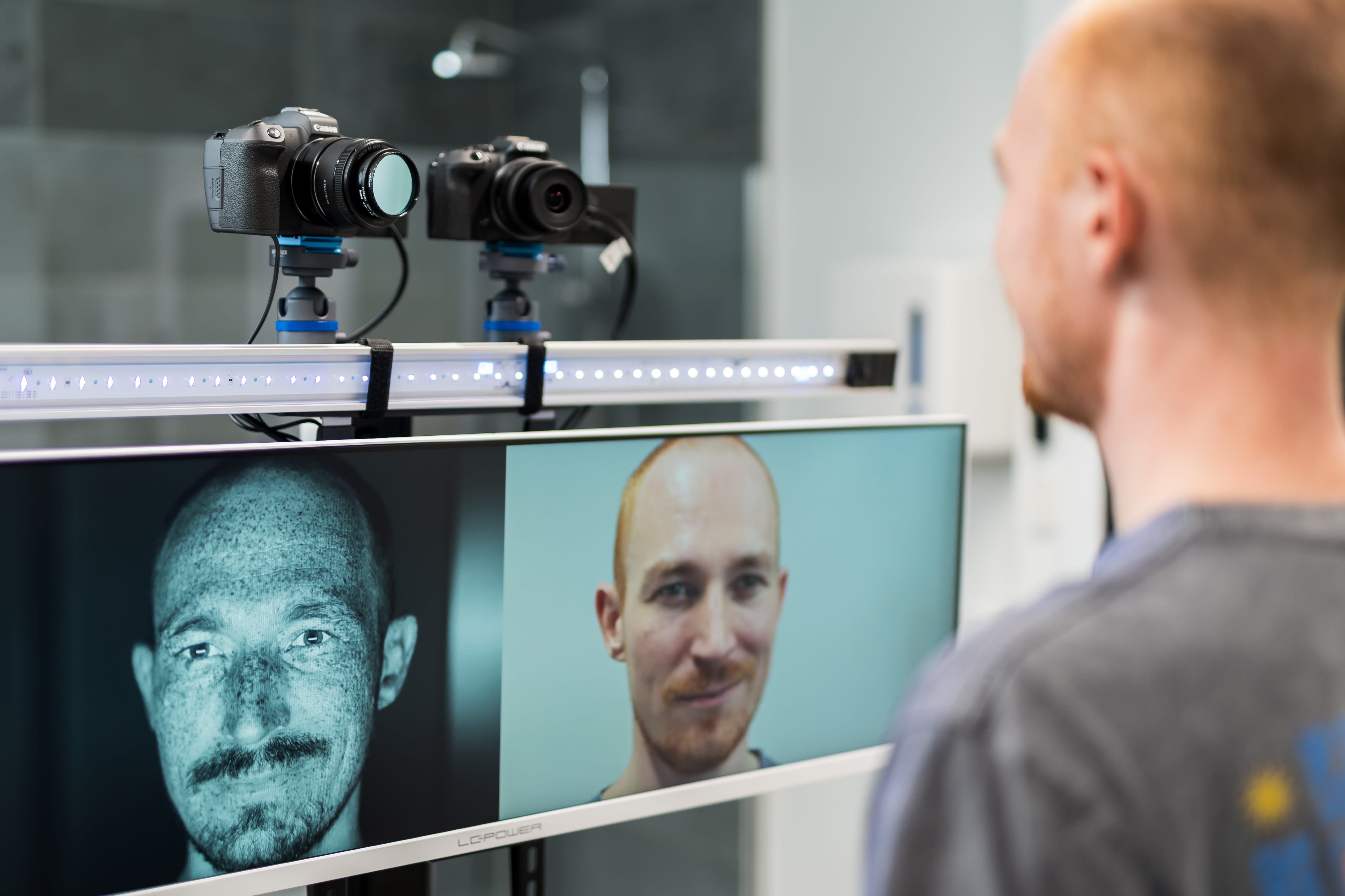 Man facing cameras with two facial images on a screen.