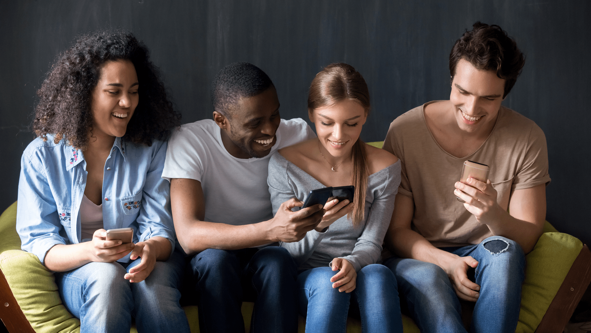 Four people sitting on a couch, looking at smartphones and smiling.