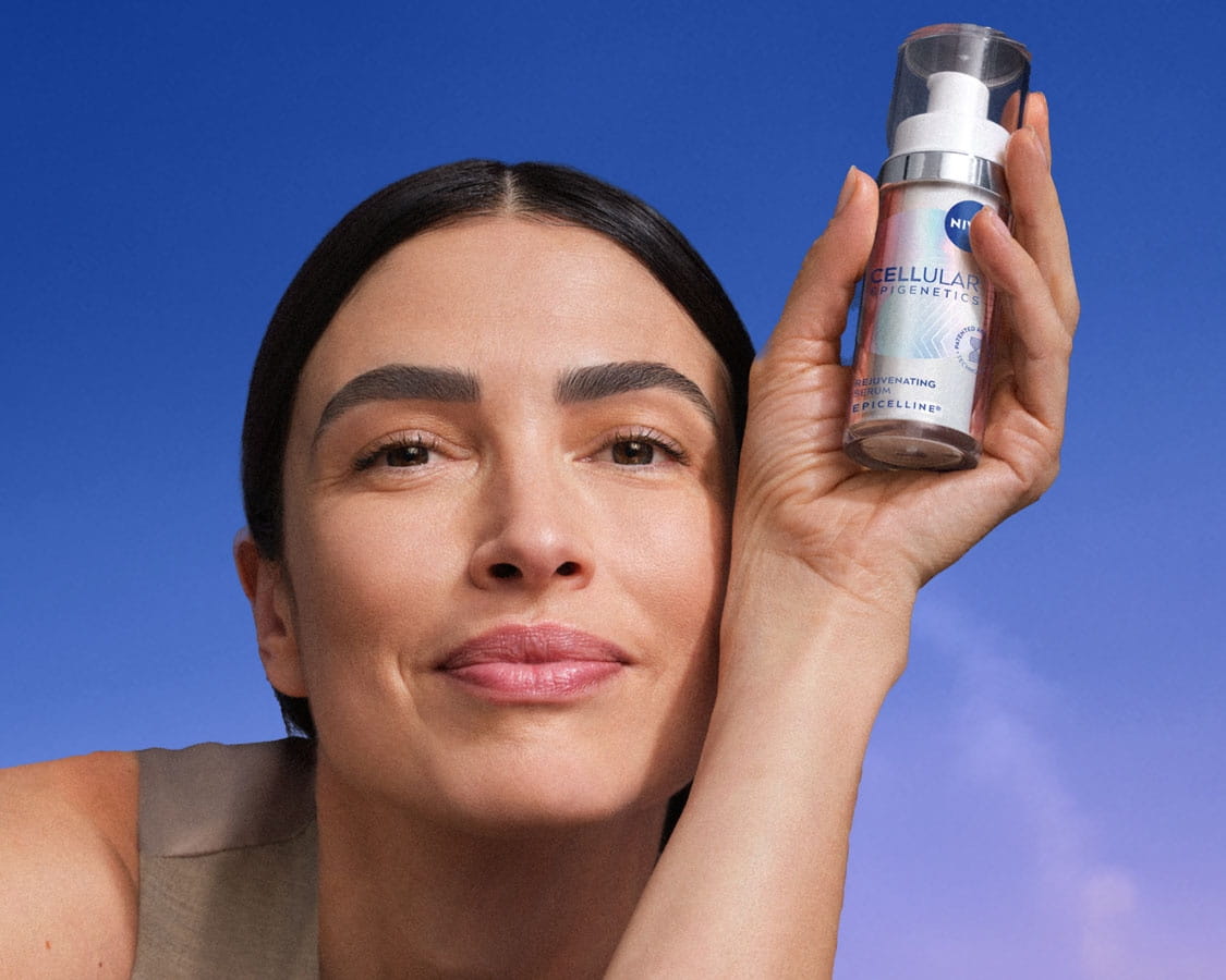 A smiling woman lounges, holding up a bottle of NIVEA CELLULAR Epigenetics - Rejuvenating Serum with EPICELLINE®.