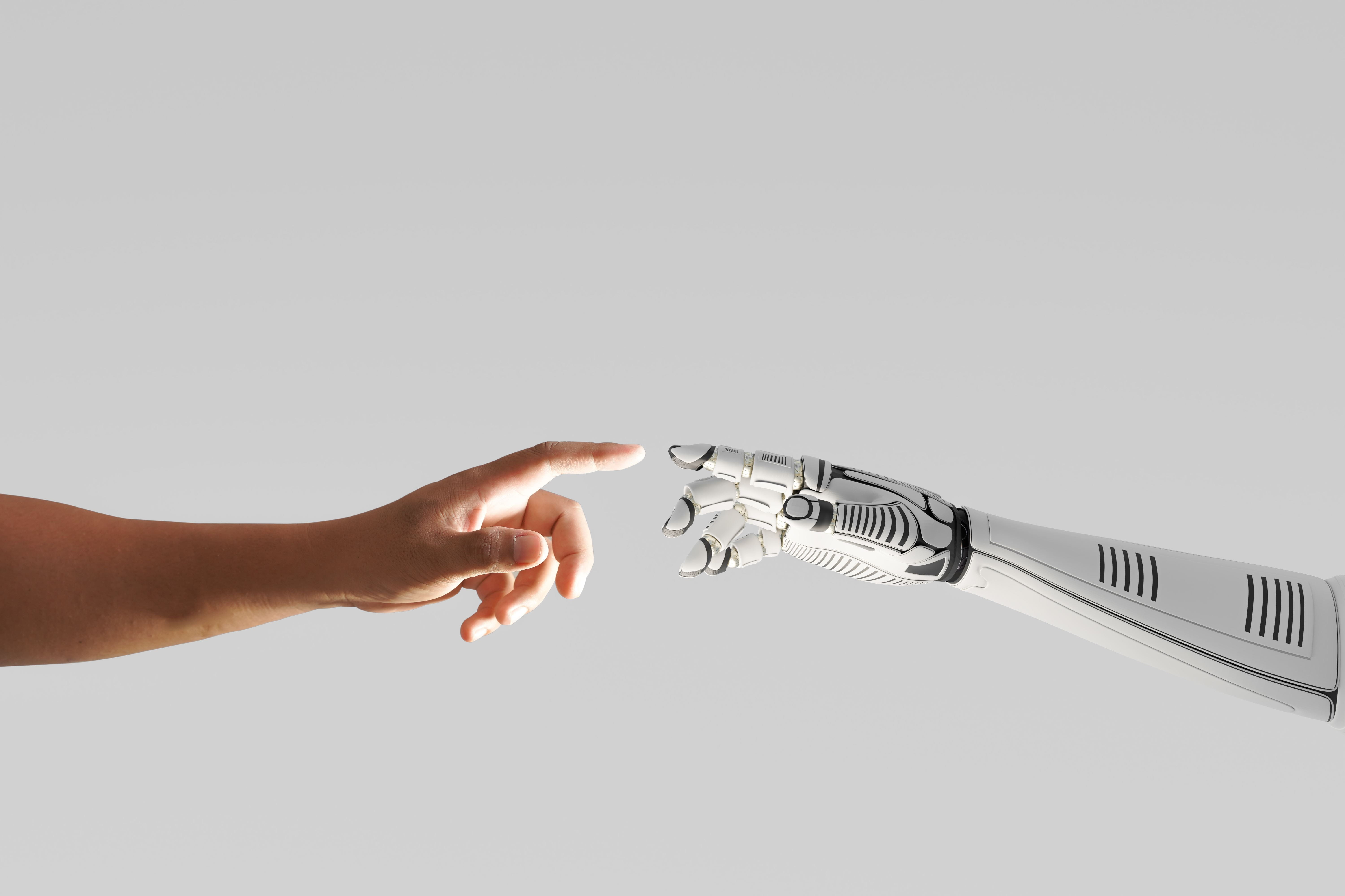 Human hand reaching towards a robotic hand on a gray background.