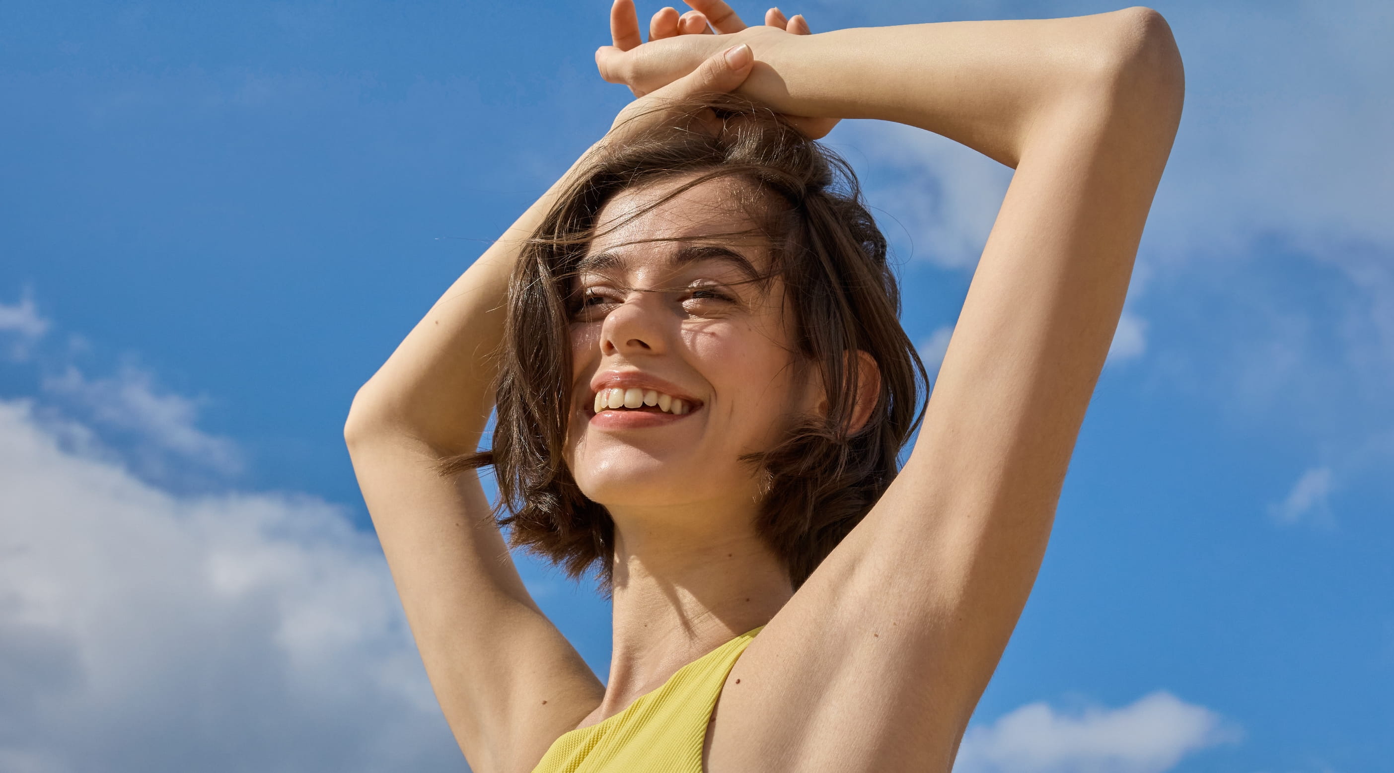 Kvinna som ler, har händerna ovanför huvudet, blå bakgrund