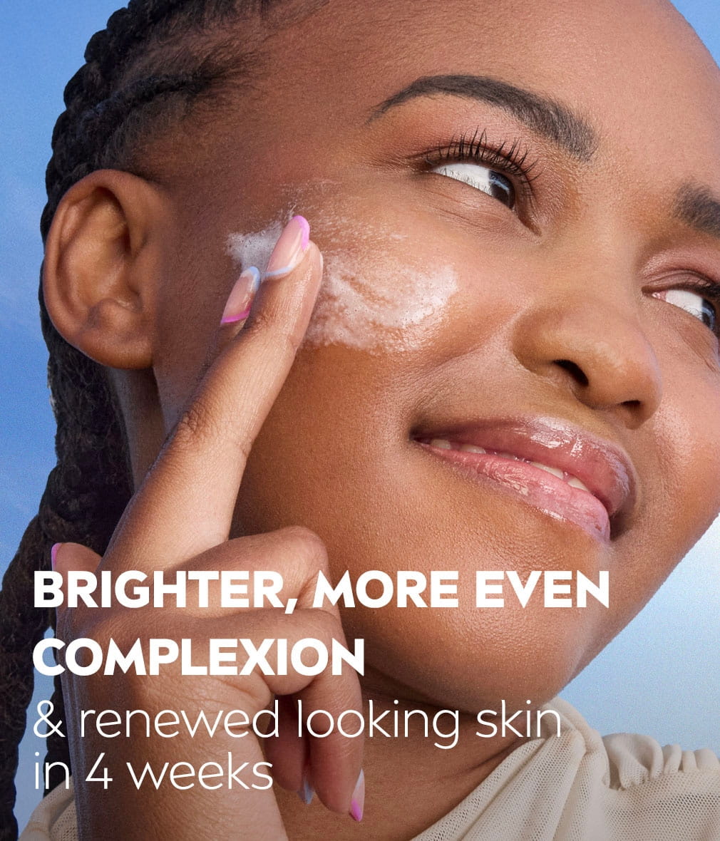 Young woman smiles, looking to the side with a hand swiping Wash Gel onto her cheek, with text describing brighter, even complexion.