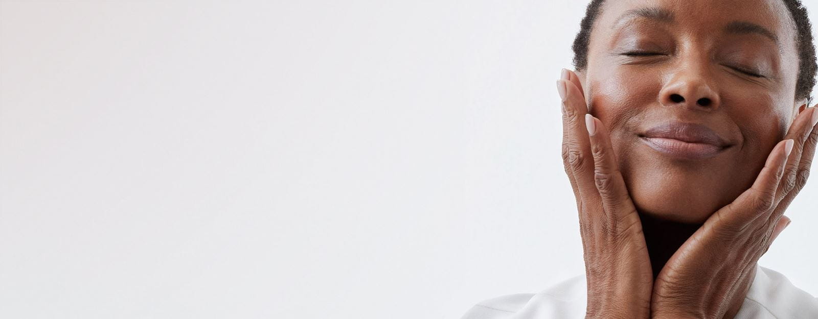 A person seen holding their face in their hands while smiling with their eyes closed.