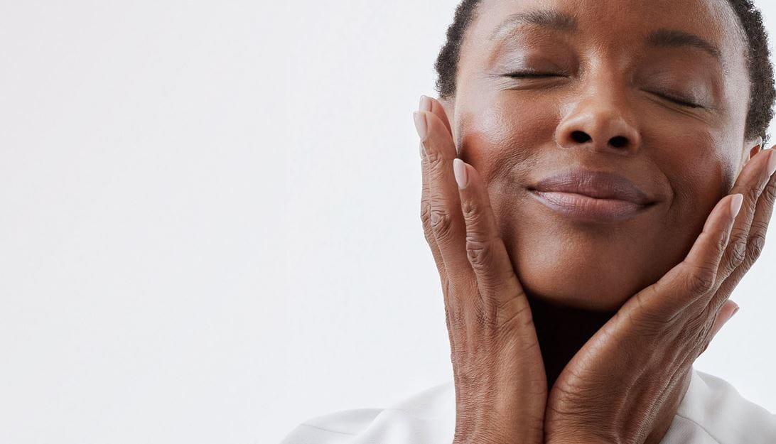 Personne se tenant le visage entre les mains et souriant les yeux fermés.