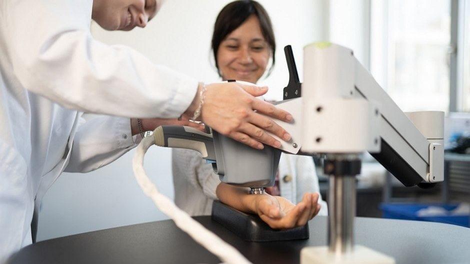 Two people using a scientific device on a forearm in a lab.