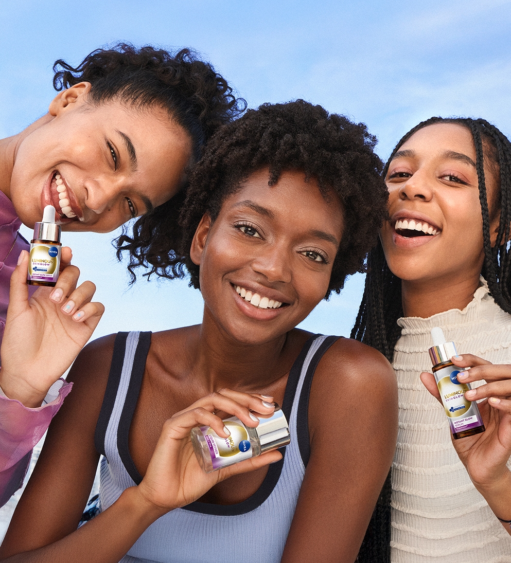 A group of laughing young women pose holding up bottles from the NIVEA LUMINOUS630® Skin Glow range for the best glow up routine